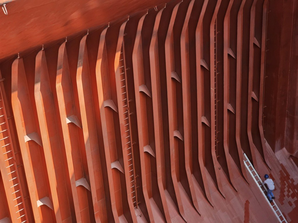Clean bulk carrier cargo hold after CARGOWARD® cleaning—epoxy-coated frames and hopper slopes inspected by an independent surveyor using a ladder.