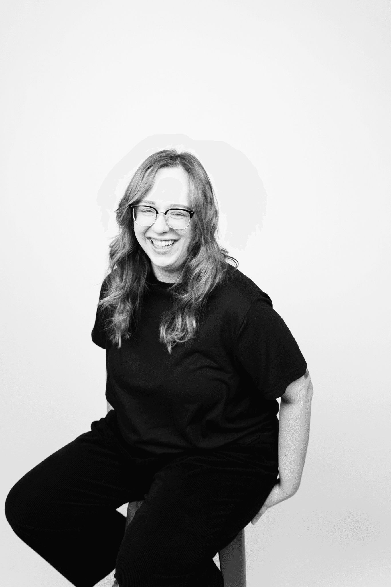 Image of Jenna: a woman with long wavy hair, glasses, and wearing an all black outfit, smiling