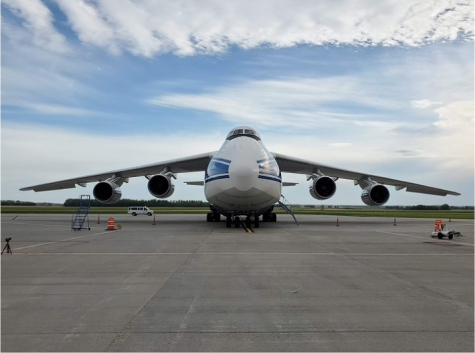 A large cargo airplane is parked on the runway, viewed from the front with a cloudy sky in the background.