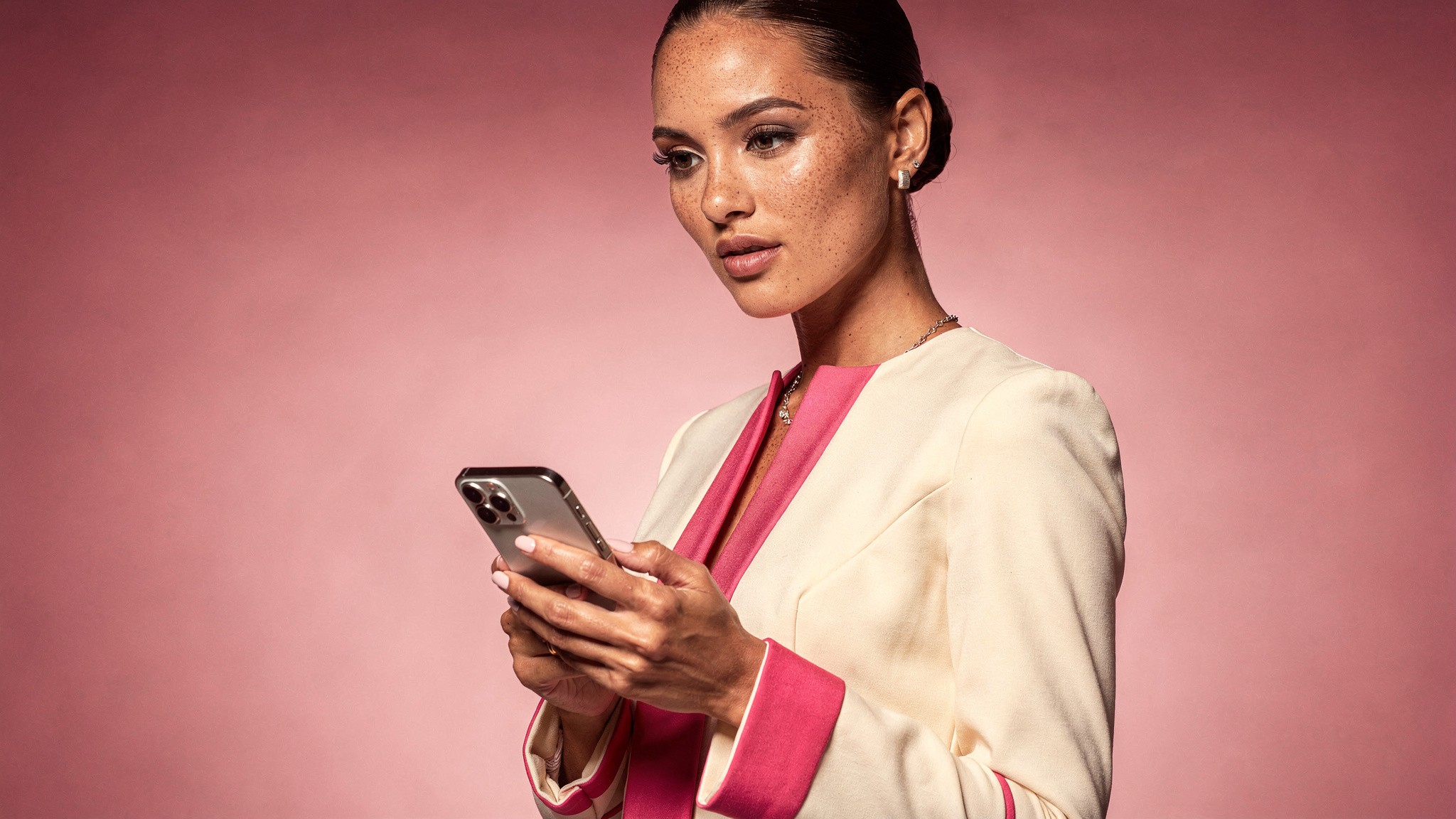 Creator looking thoughtfully at her phone in a pink studio, ai photos of yourself mistakes