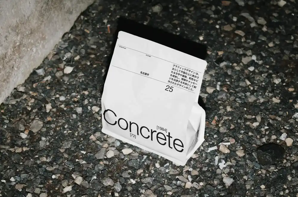 Bold red product packaging mockup for "Concrete," displayed on a gravel surface. Features minimal black typography, subtle geometric design, and Japanese text, evoking an industrial, modern aesthetic.