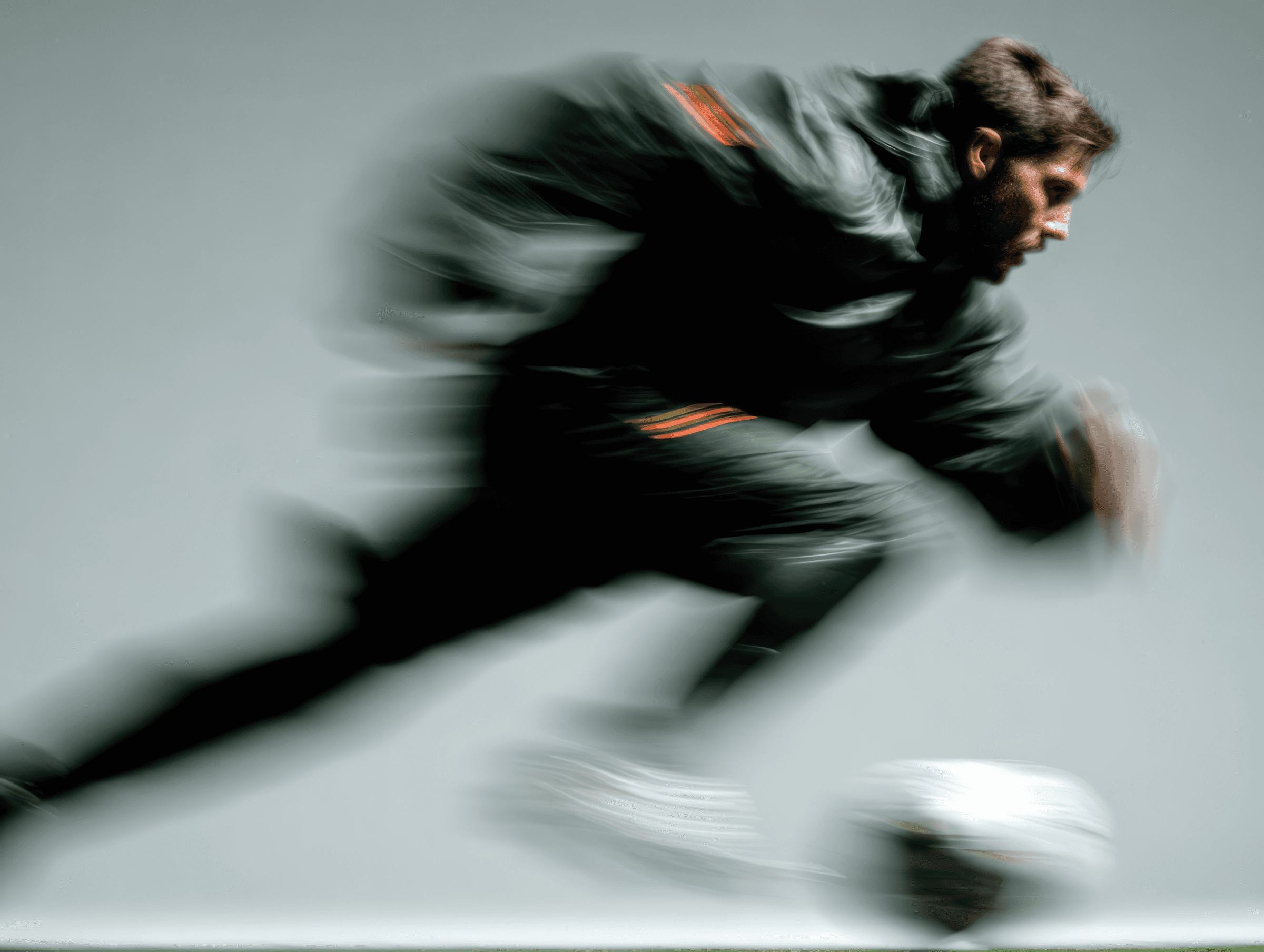 Man in a dark tracksuit sprinting past a blurred soccer ball in motion