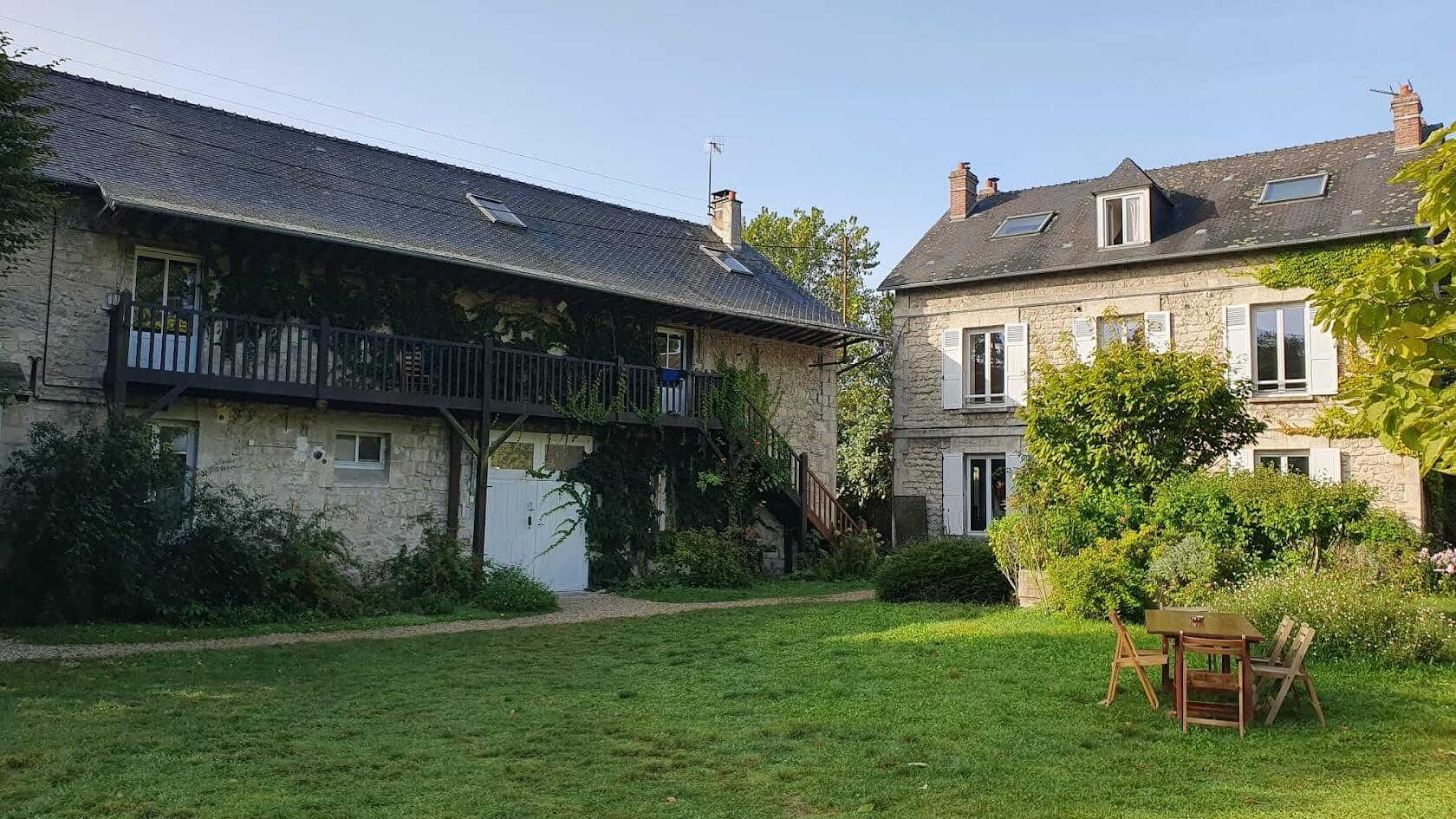 Vue ensoleillée de deux charmants bâtiments entourés de verdure et de plantes dans un cadre extérieur paisible.