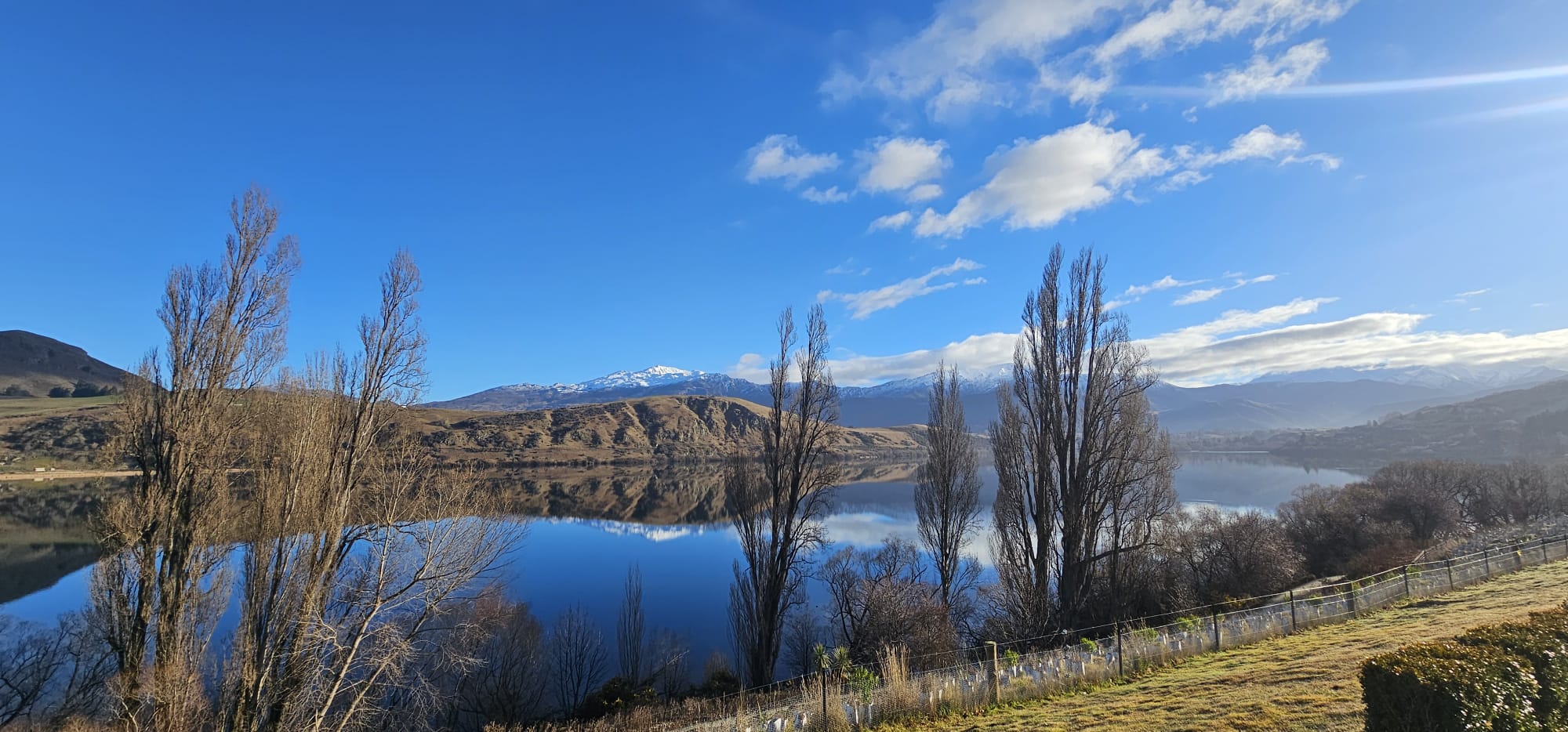 Un lago rodeado de montañas y árboles en el sur de Nueva Zelanda bajo un cielo azul.