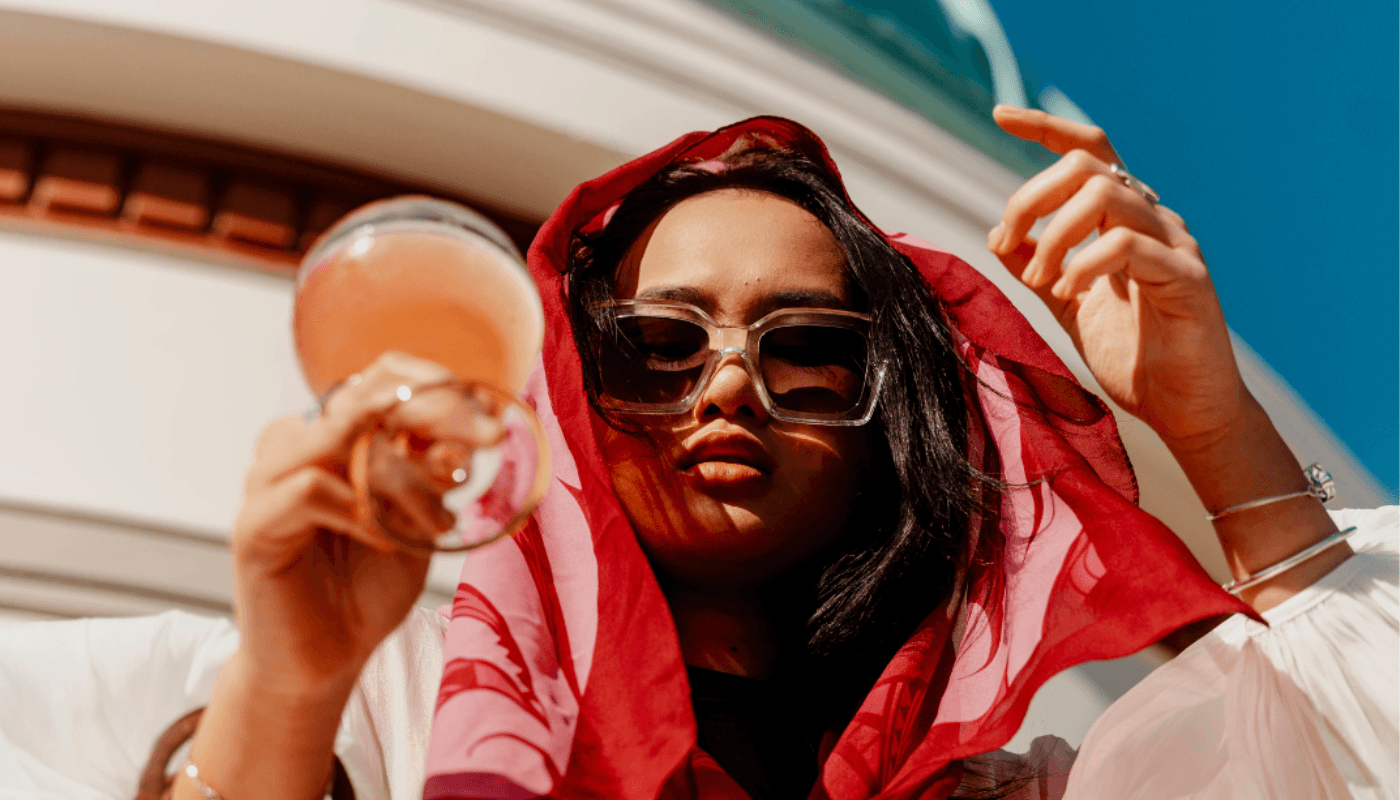 Woman in sunglasses and a red scarf holding a pink cocktail in the sunny Hawke's Bay.