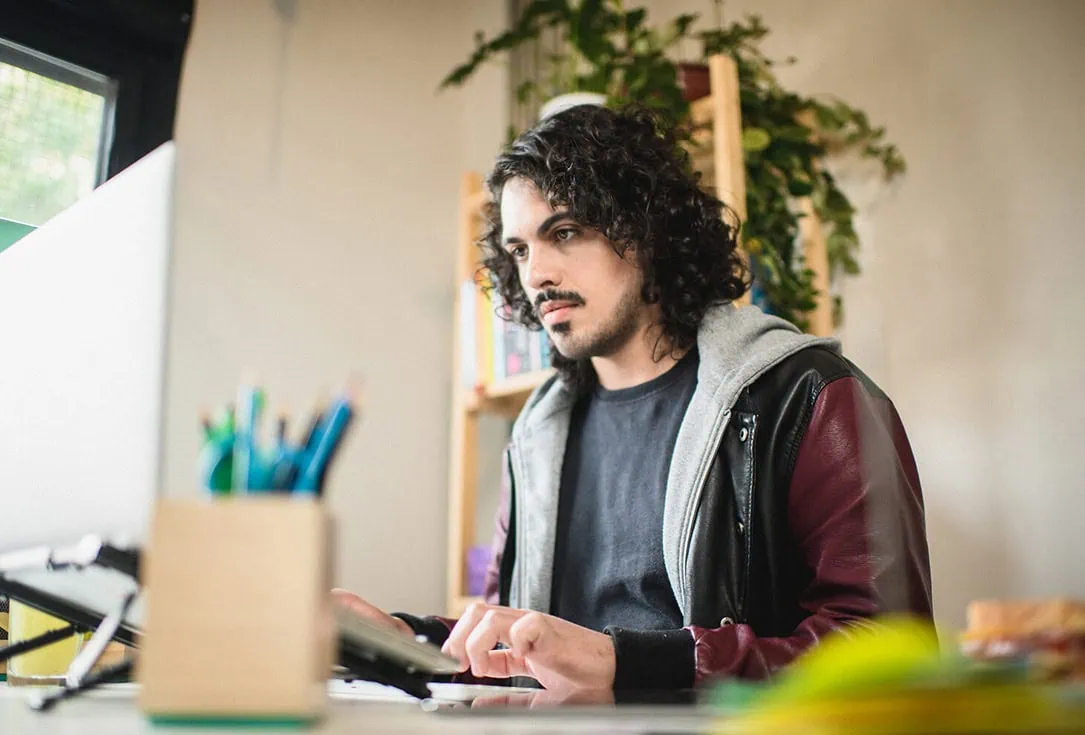 Homem de cabelo enrolado trabalhando em um laptop estudando com a Tera
