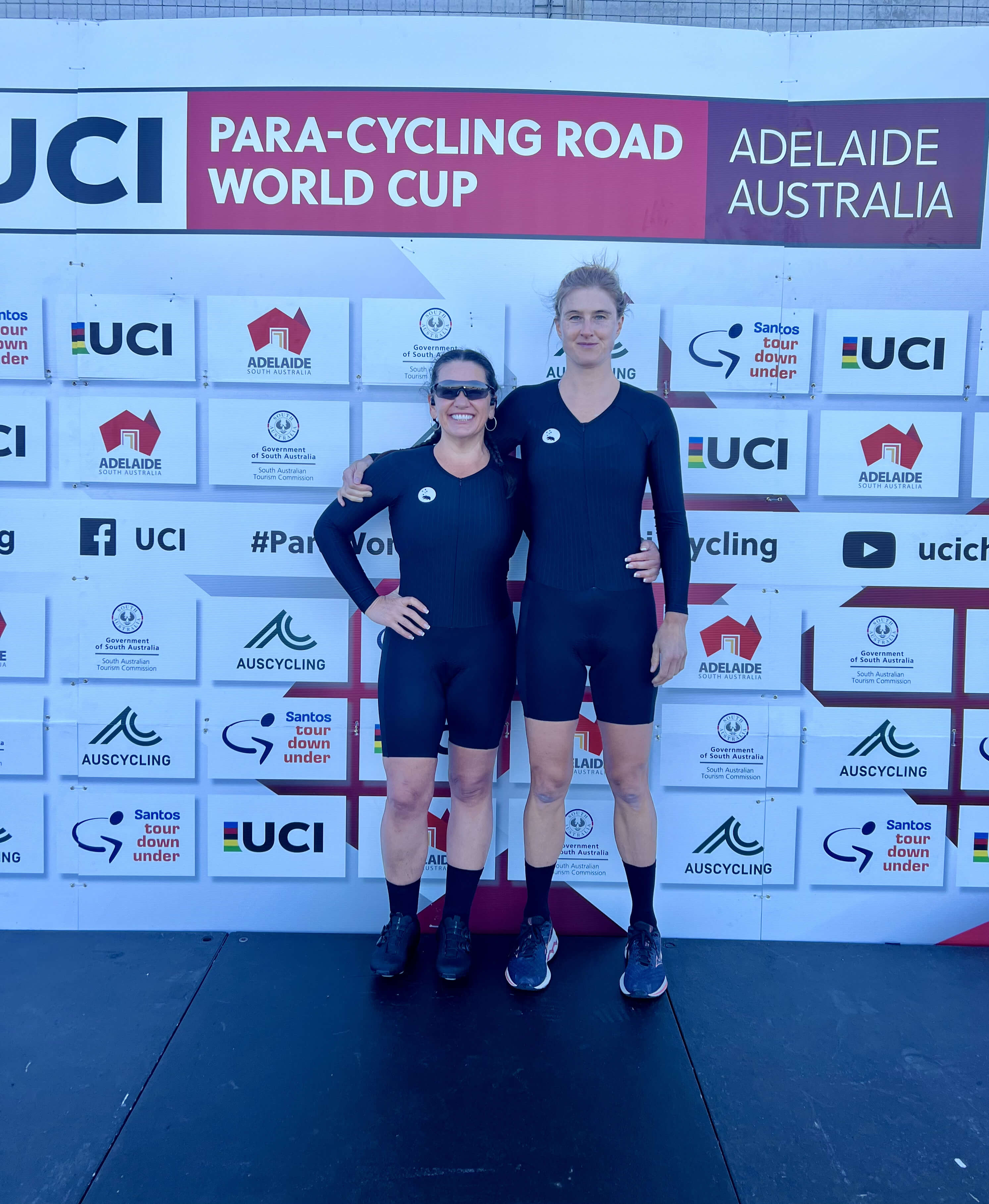 Lily and Jay pose on the podium at the para-cycling world cup in Adelaide pre-race. They wear their black time trial cycling kits.