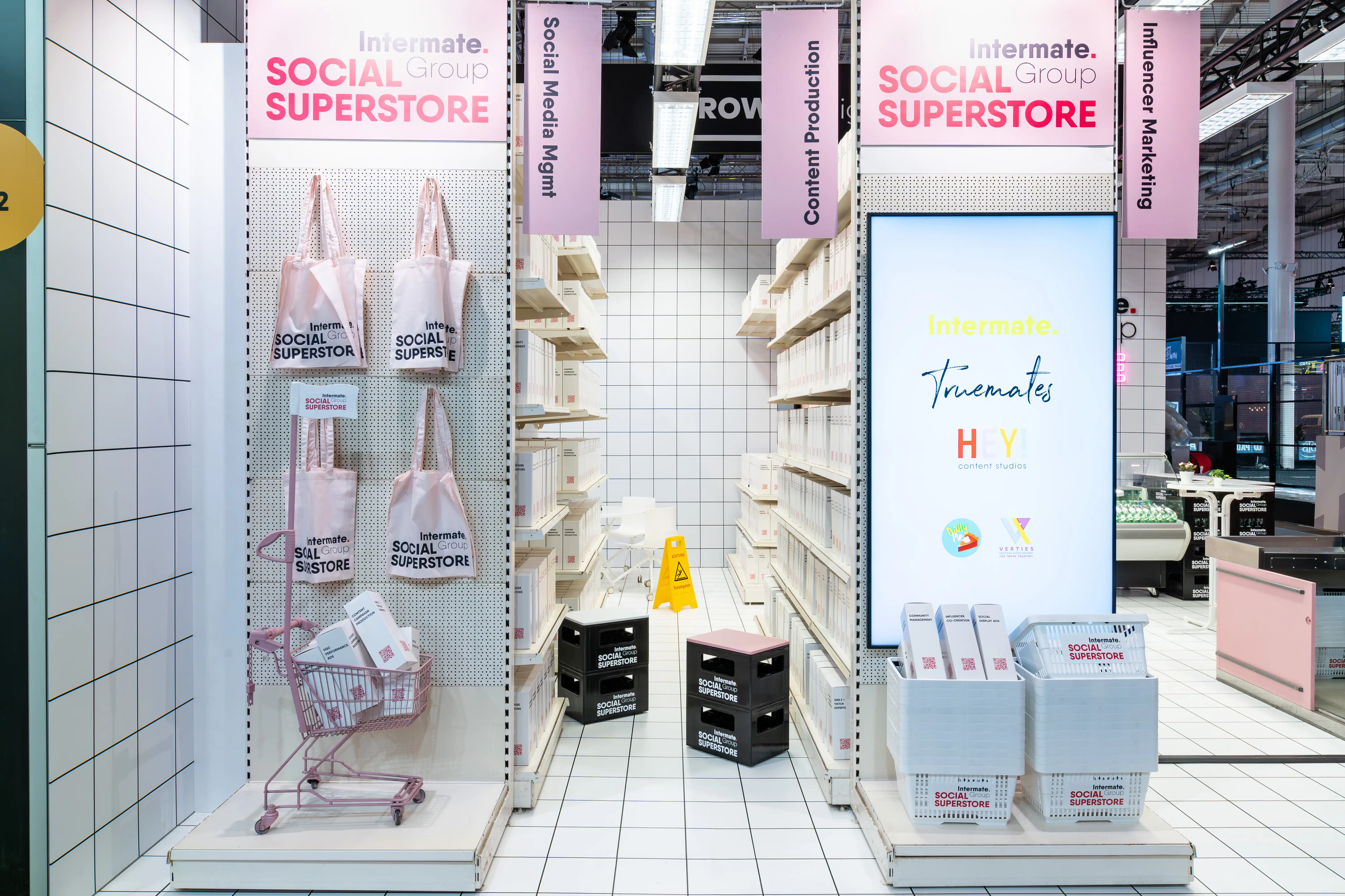 Shelf displays with pink tote bags, shopping cart and service signage at the Intermate Social Superstore.