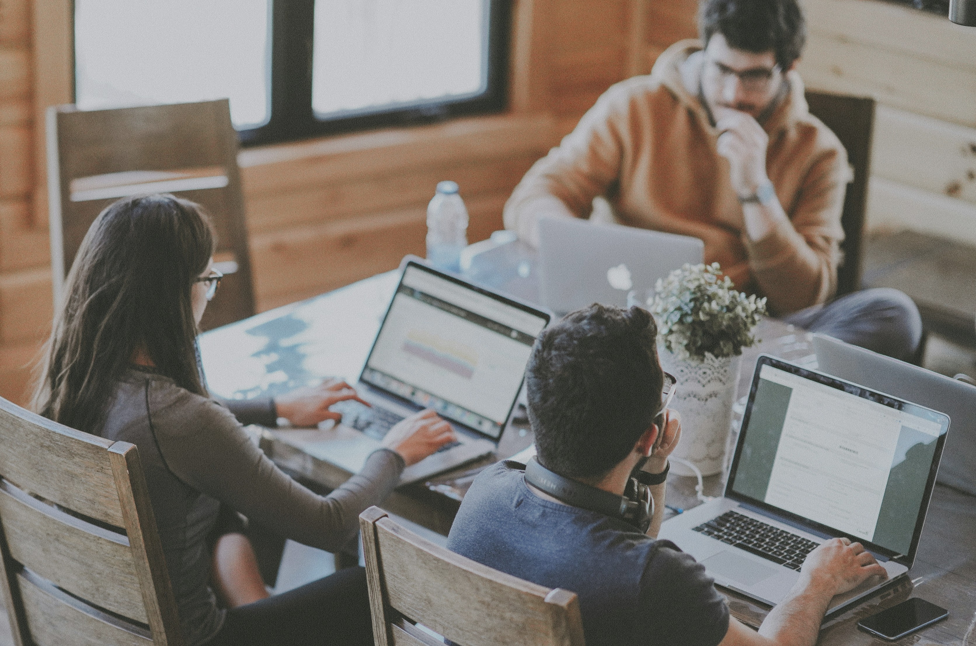 Three people working on laptops at a shared wooden table