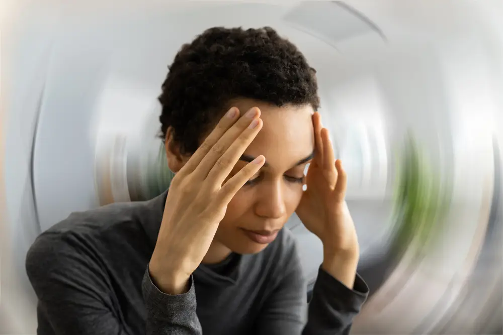 A person sits with their hands on their head, appearing stressed or in deep thought. Background is blurred.