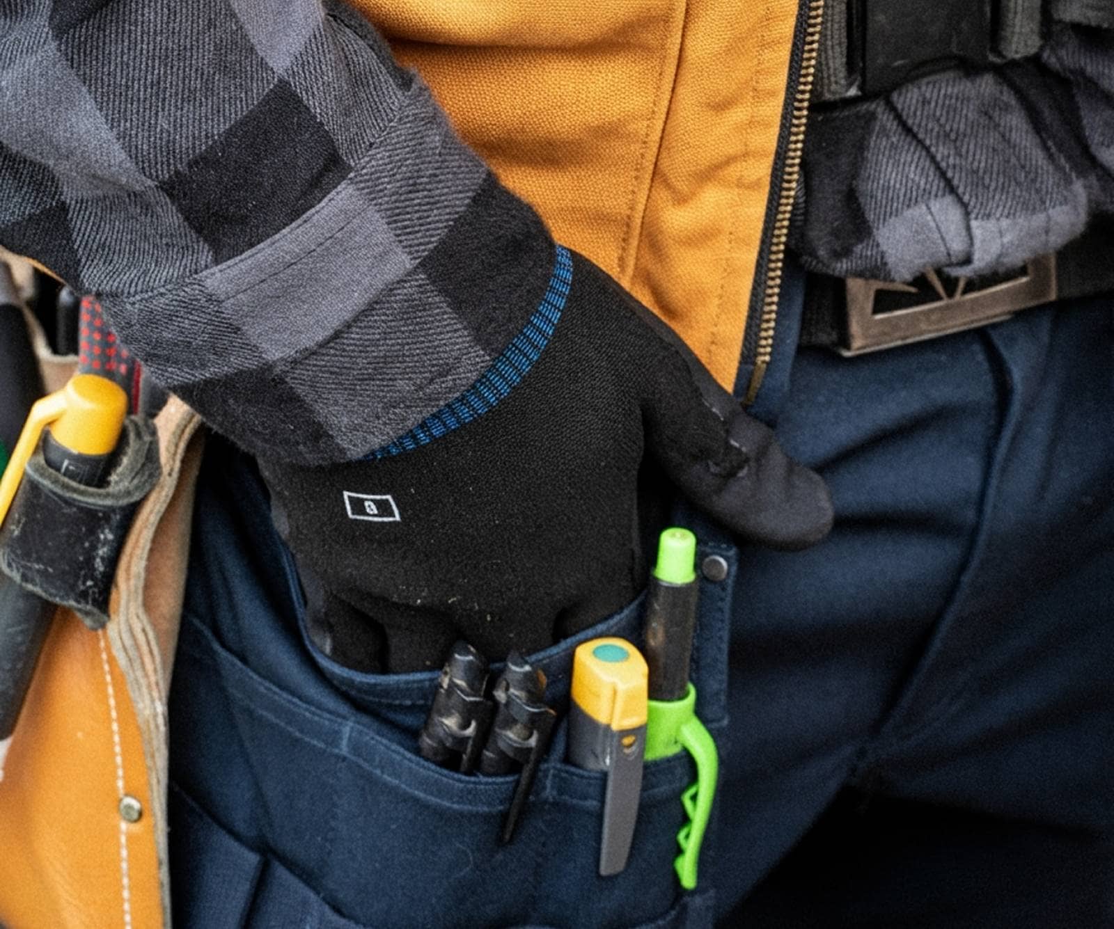 A young person with curly hair smiles at the camera while sitting in front of a laptop against a dark background.