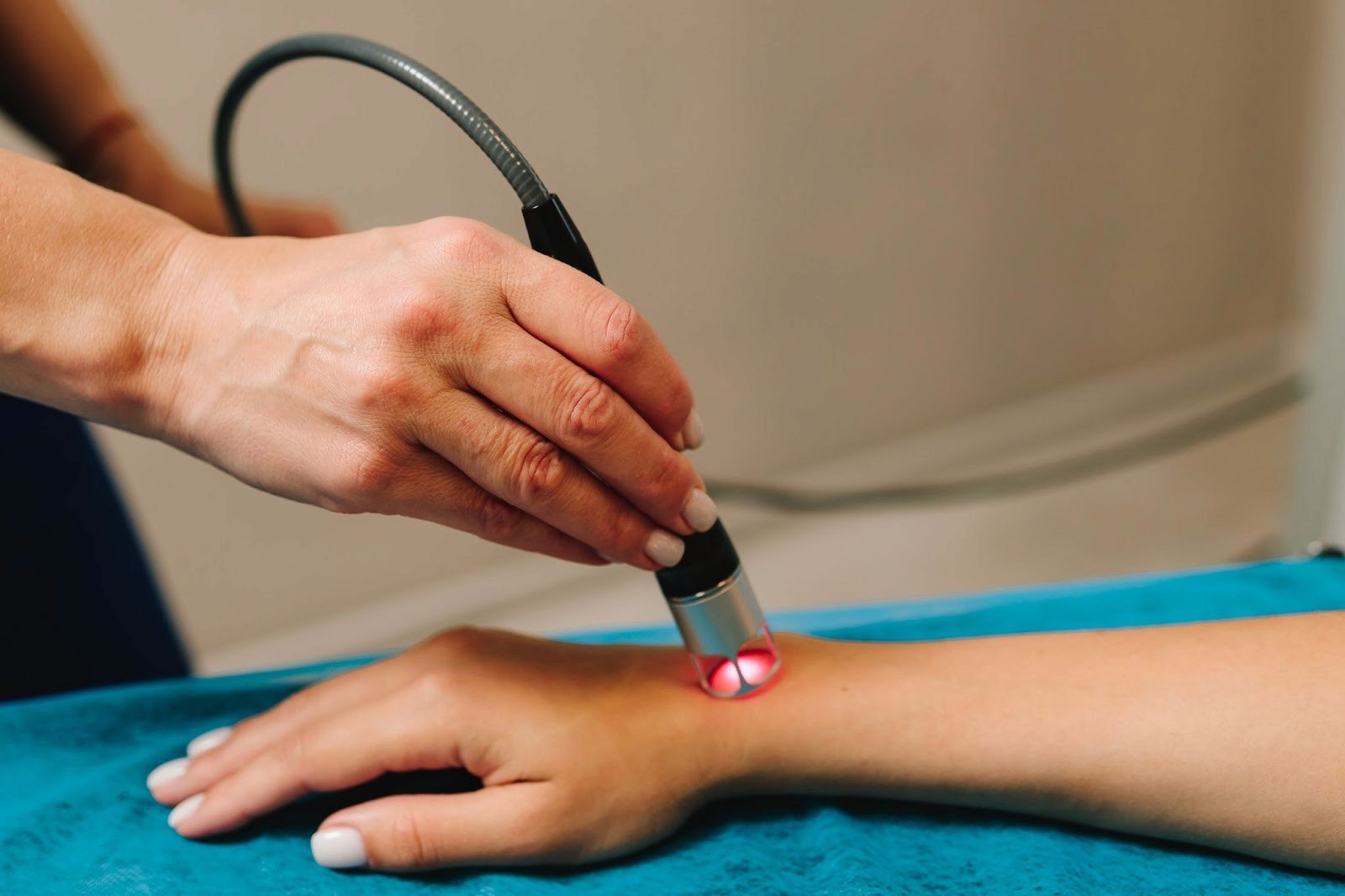A medical professional using a laser therapy device on a patient's wrist.