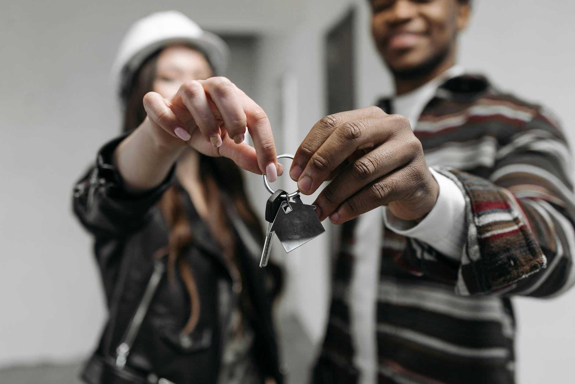 A man and woman holding out a house key together towards the camera in a light interior