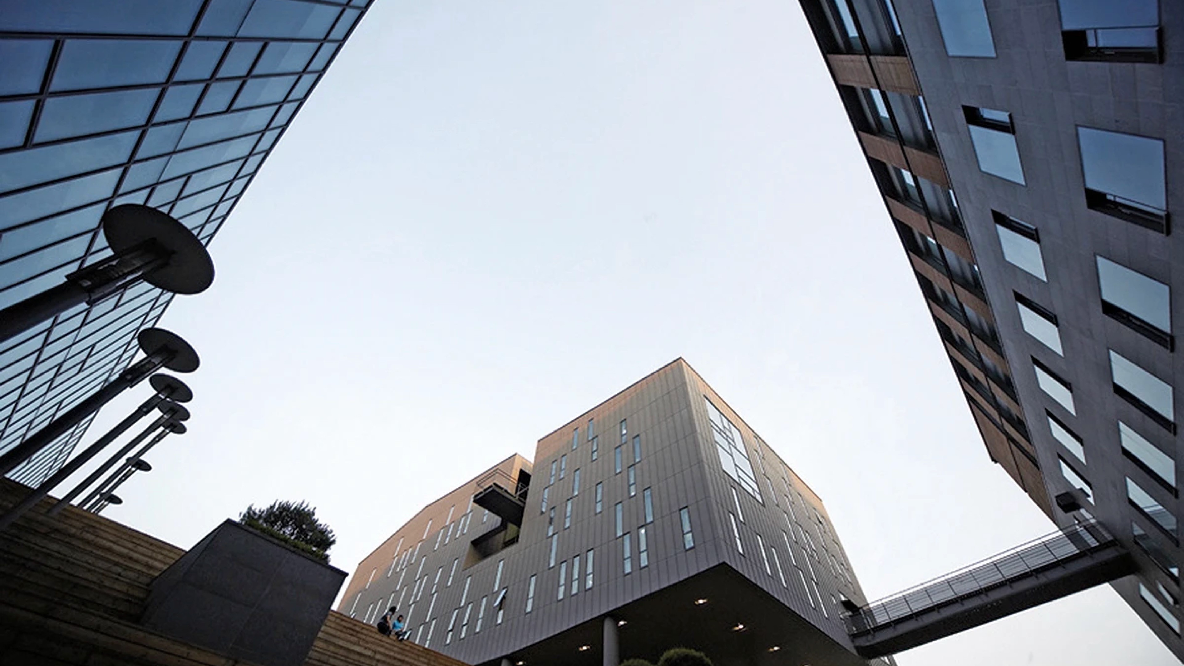 숭실대학교 캠퍼스 건물을 아래에서 위로 올려다본 앙각 구도 사진. 유리 커튼월 외관의 현대식 건물들 사이로 맑은 하늘이 보이며, 독특한 형태의 가로등이 좌측에 배치되어 있다. 2027학년도 숭실대학교 영화예술전공 연출 입시 정보 안내 이미지.