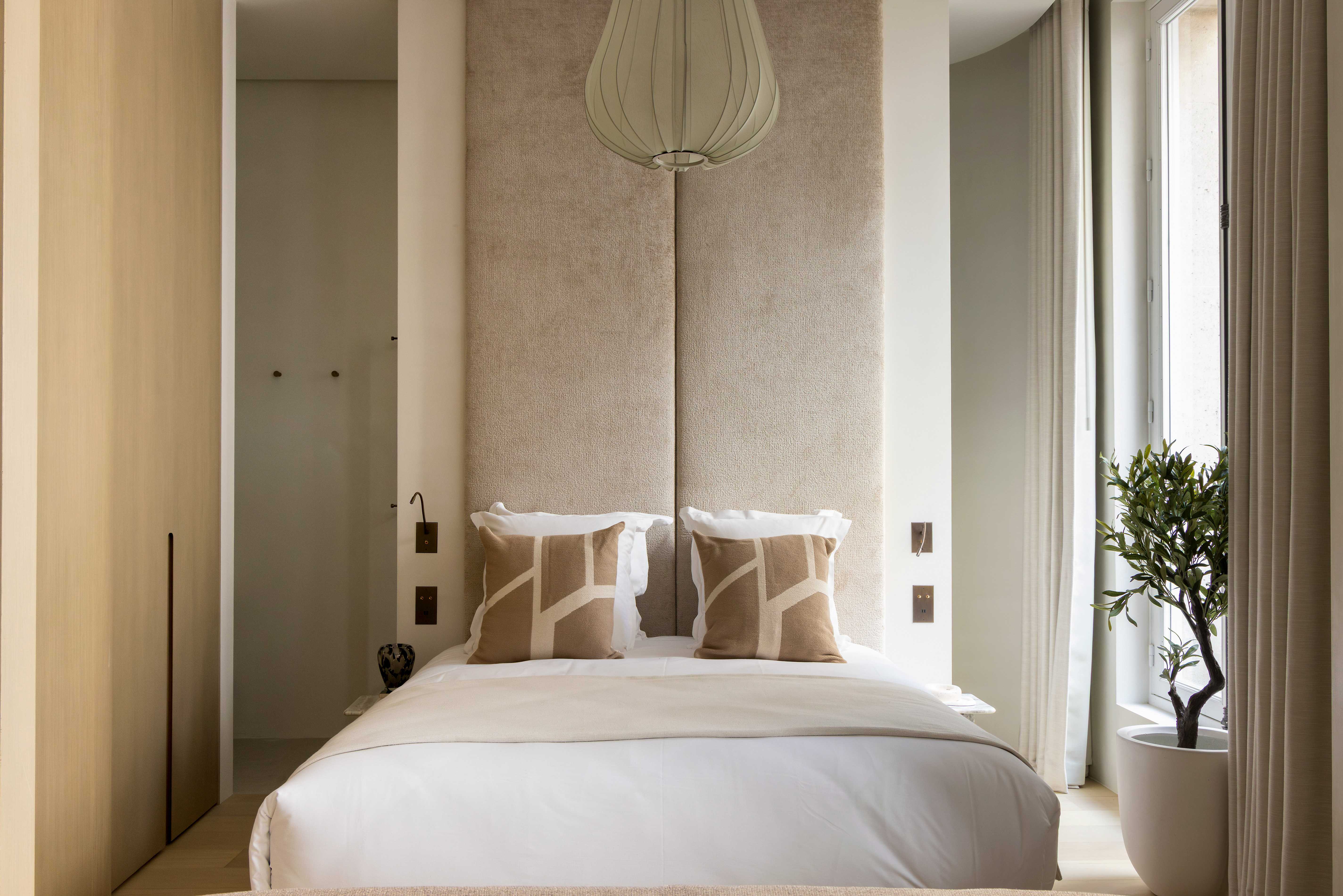 Chambre avec lit double, tete de lit haute en velours sable, suspension design et olivier en pot pres de la fenetre