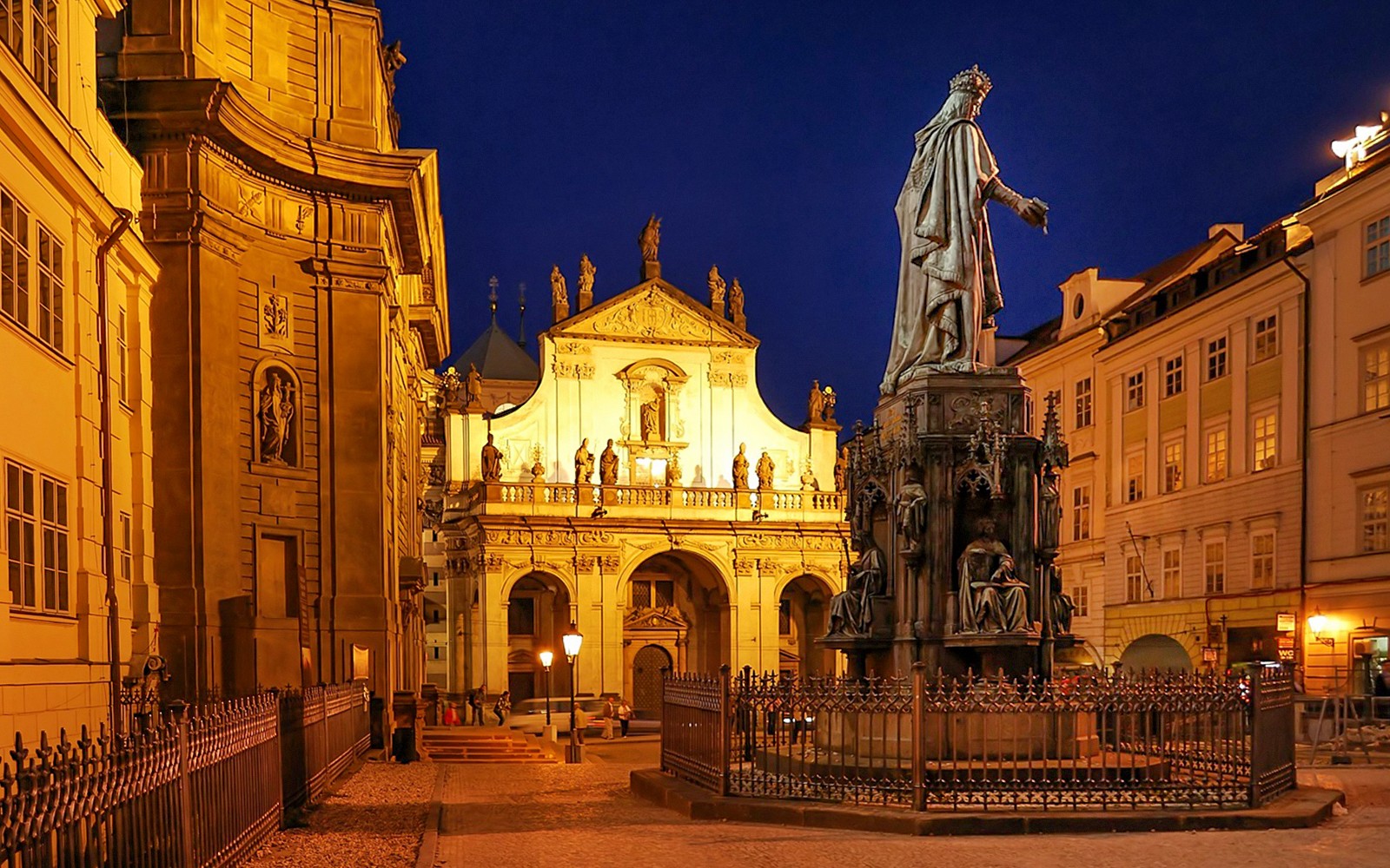 夜晚的布拉格中世纪街道，灯光映照着雕像和历史建筑。