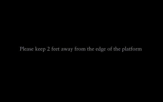The image displays a black background with white text that reads: "Please keep 2 feet away from the edge of the platform."