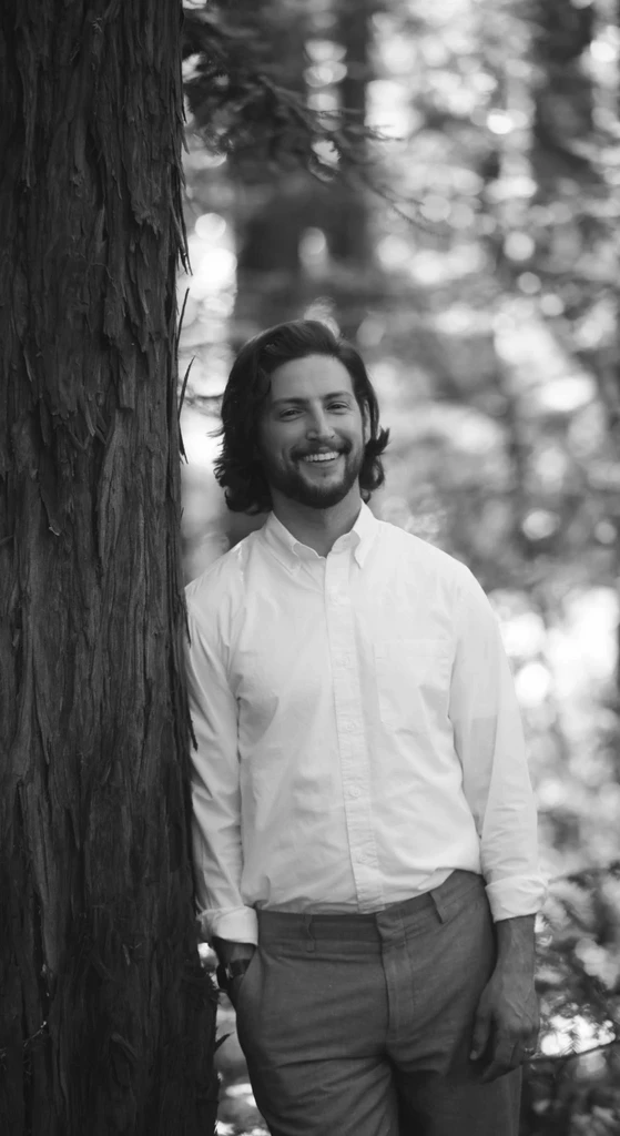 Man smiling and standing next to a redwood tree