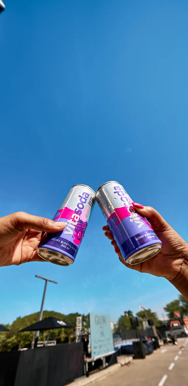 Two cans of Vita Soda Glow touched together against a blue sky