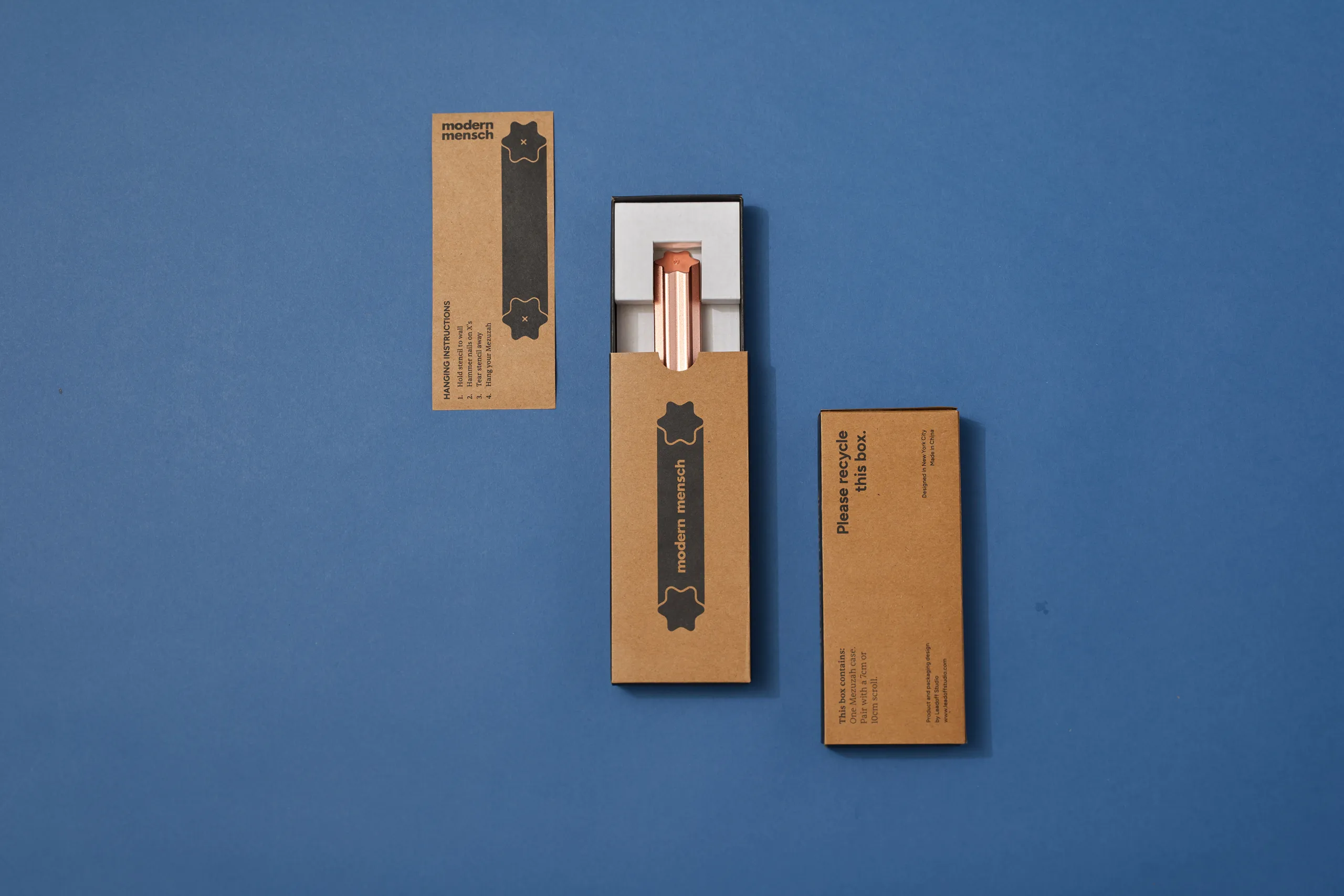 Modern Mensch Mezuzah packaging components arranged on a blue background