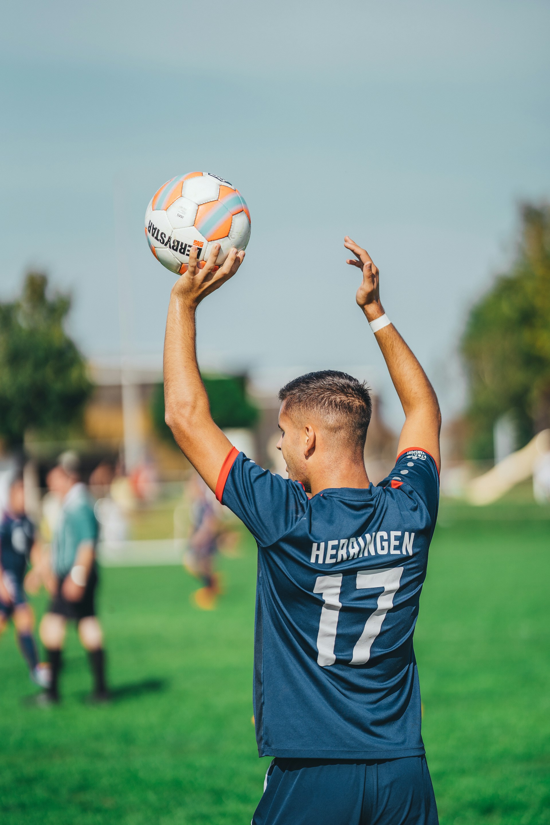 Rear view of a soccer player in a dark blue jersey (number 17) preparing to take a throw-in.