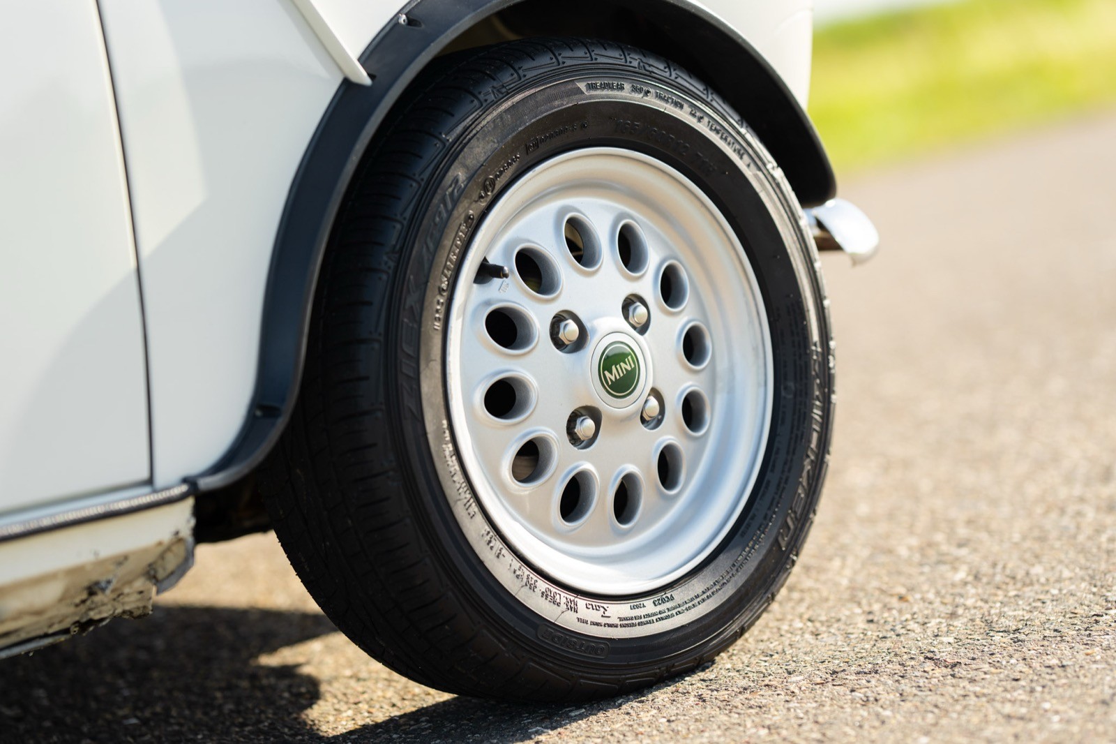 A close-up of a silver car wheel featuring multiple circular holes in the rim, positioned on a paved surface.