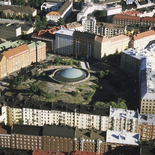 Ilmakuva kaupunkialueesta, jossa on suuri, pyöreä rakennus kupukaton kanssa, jota ympäröivät asuinrakennukset.