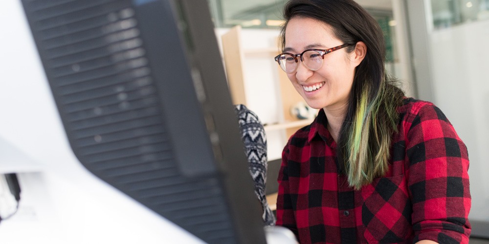 A women standing a front of a computer and smiling.