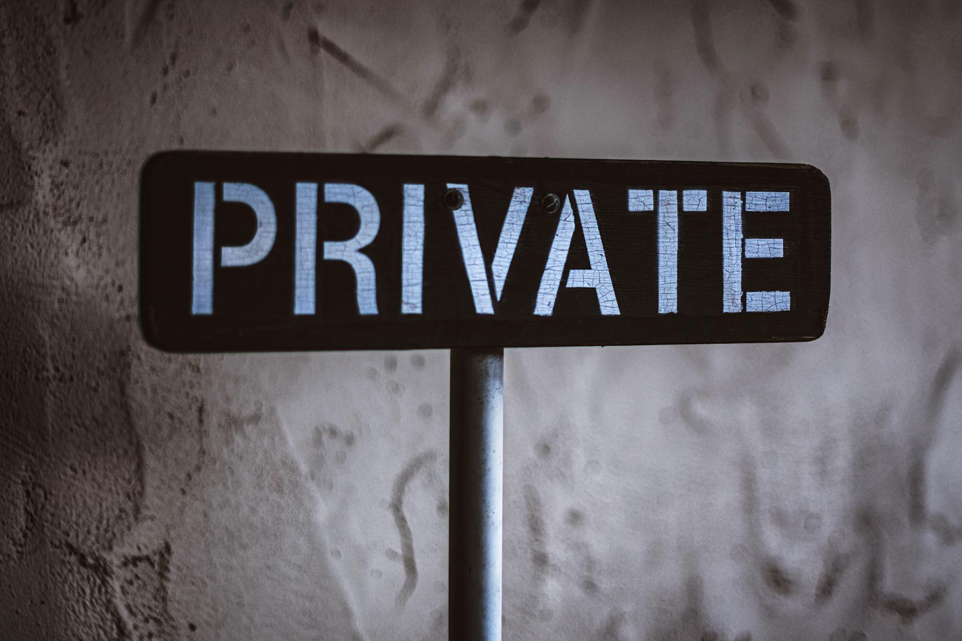 Metal PRIVATE sign on a pole against a weathered grey concrete wall