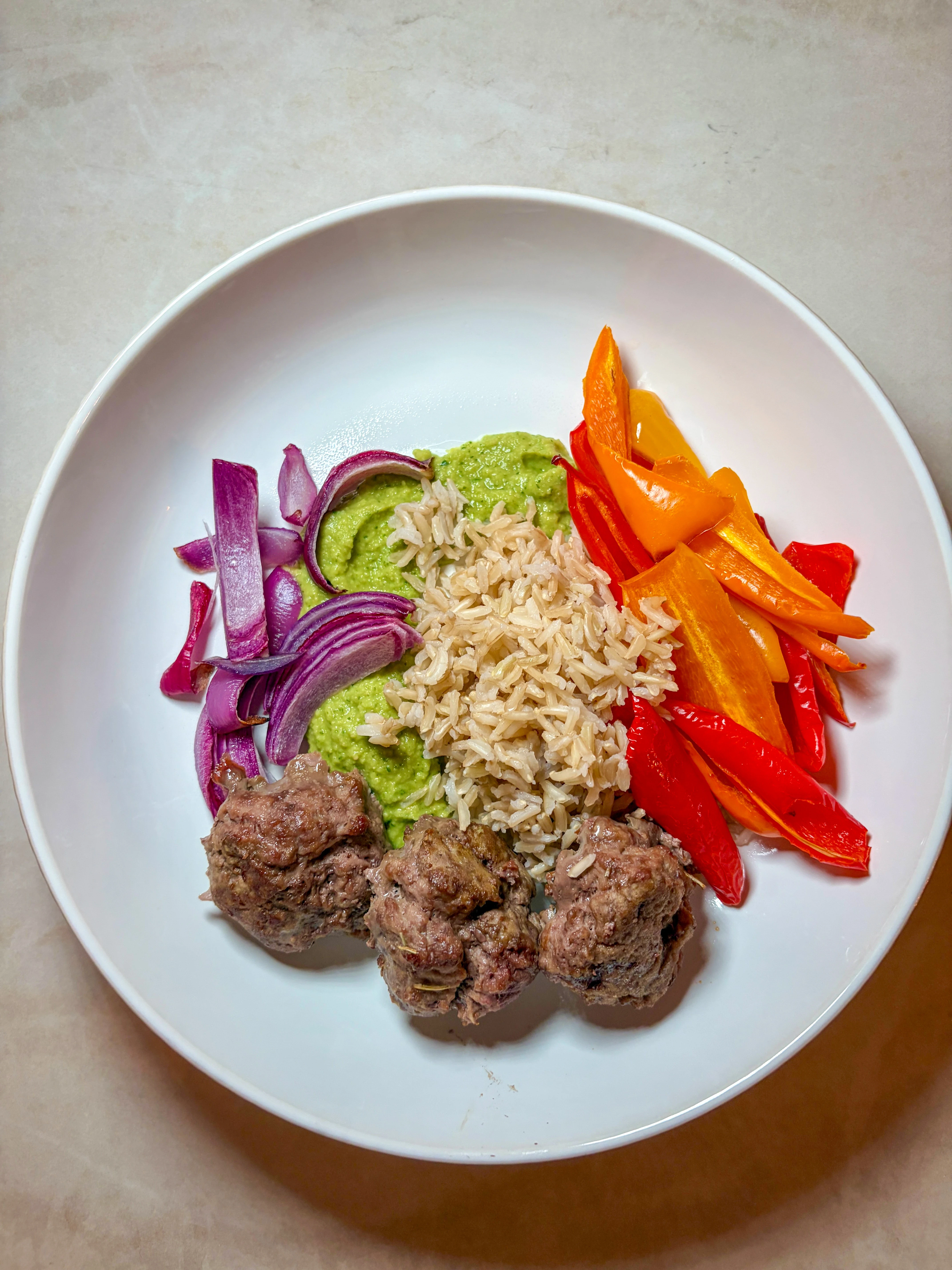 A Mediterranean bowl with meatballs, onions, rice, green parsley hummus, and red bell peppers