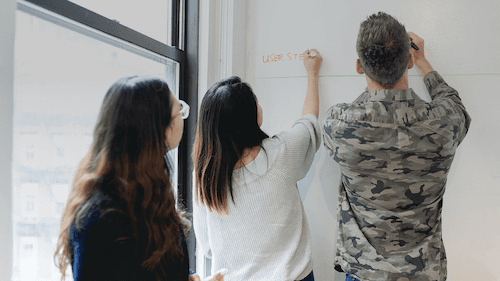 Three designers working on a whiteboard wall.