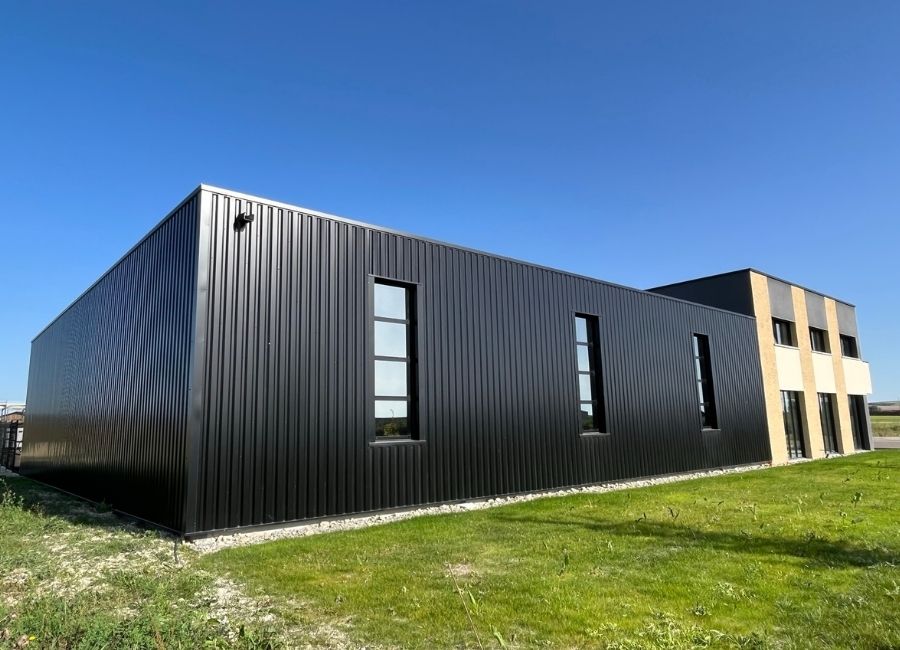 Façade moderne en bardage noir d’un bâtiment tertiaire en zone industrielle.