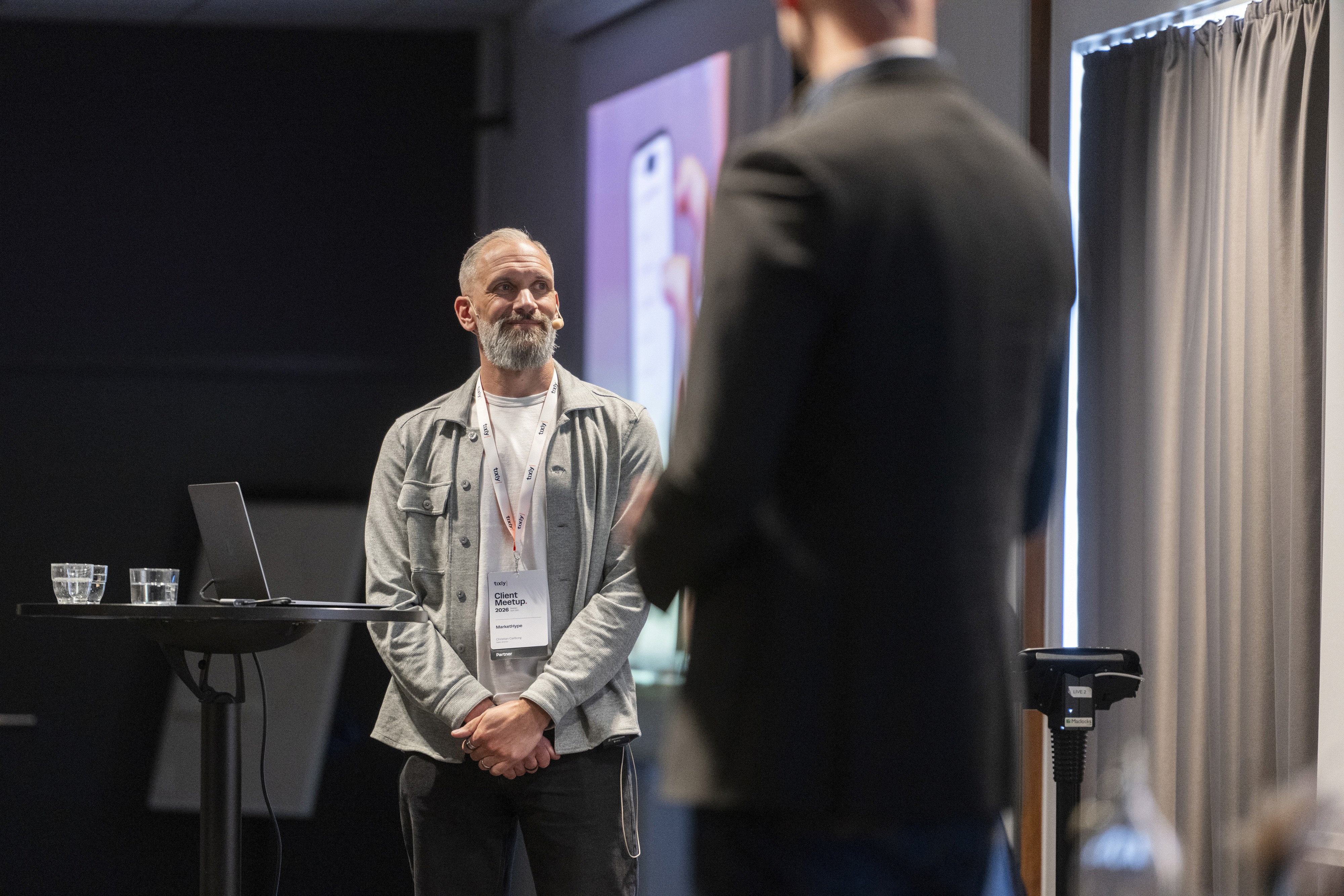 A speaker stands facing an audience member, engaged in discussion in a conference setting.