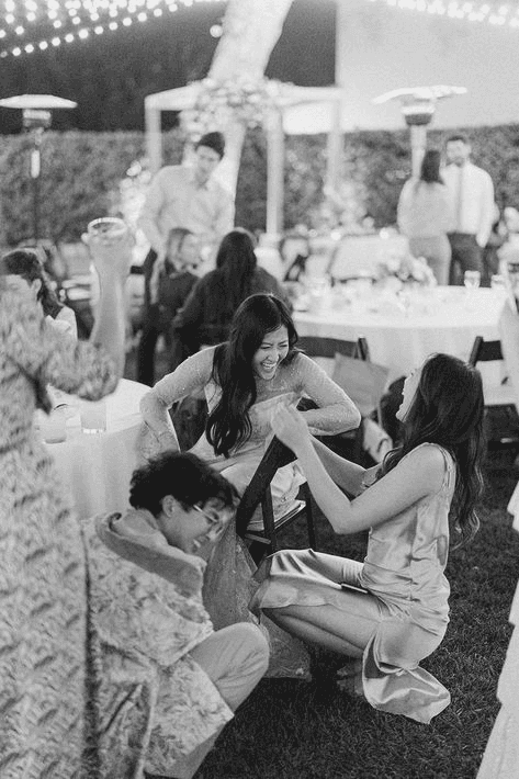 Playful and candid black-and-white shot of wedding guests laughing and interacting during the reception, illustrating the fun and light-hearted moments in candid wedding photography.