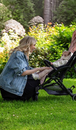 A young mum in a park, bending down and playing with her baby in a buggy