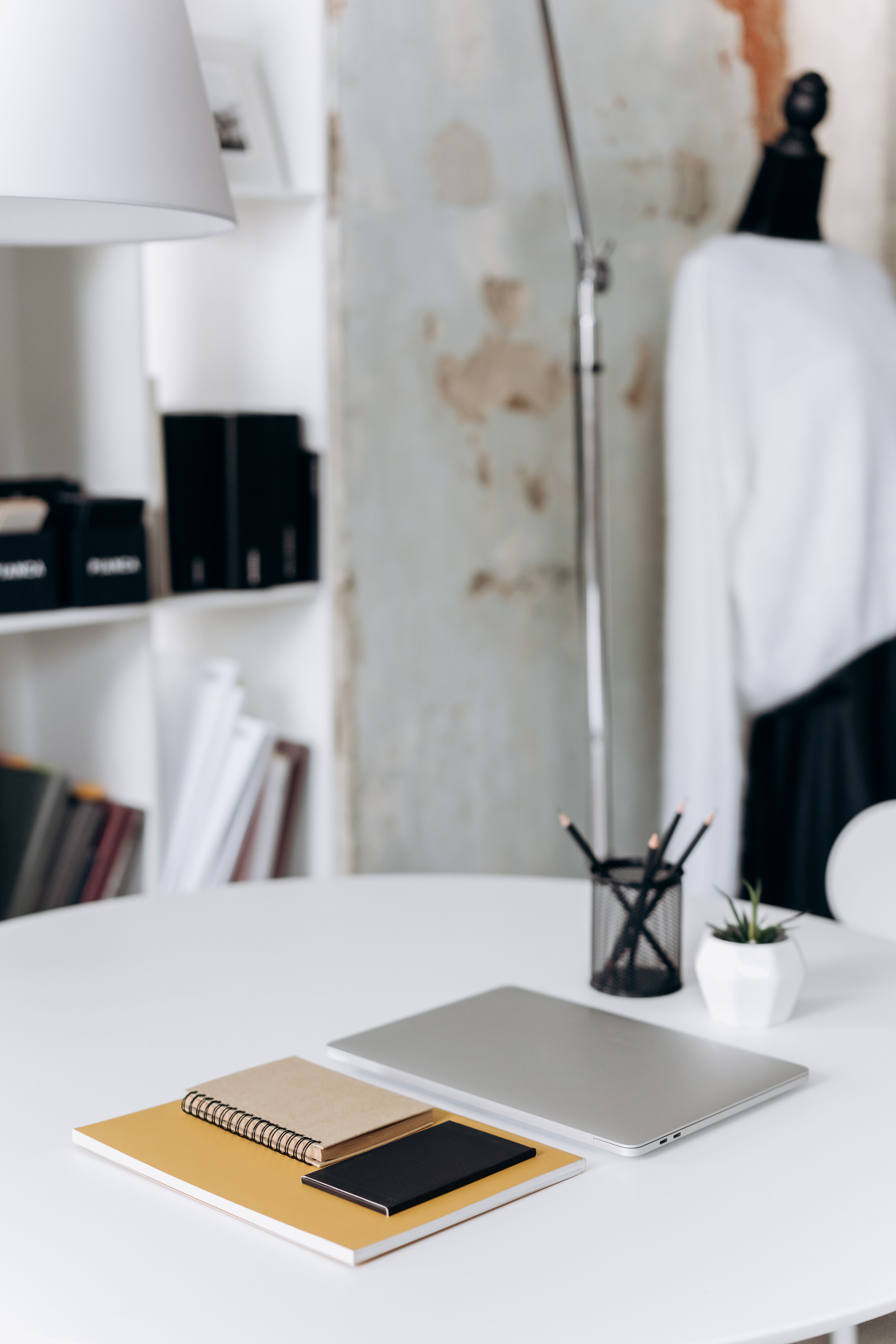 Stylish minimalist workspace featuring a laptop, notebooks, and potted plant on a white desk.