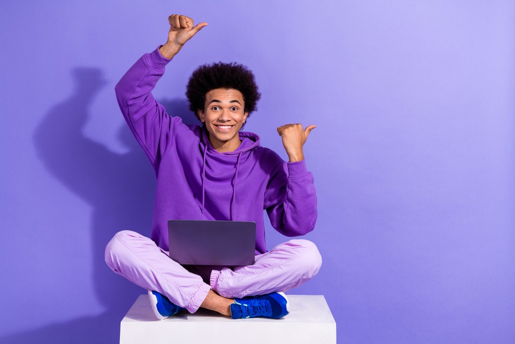 a man sitting cross legged with his legs crossed and pointing at a laptop