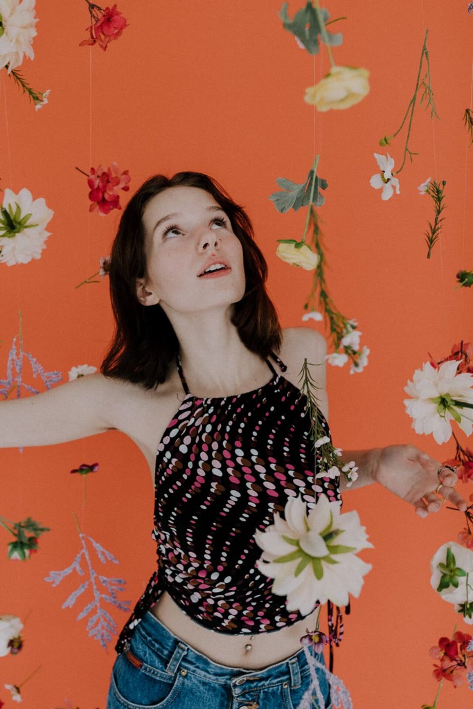 Woman looking up at the flower waterfall with orange backdrop