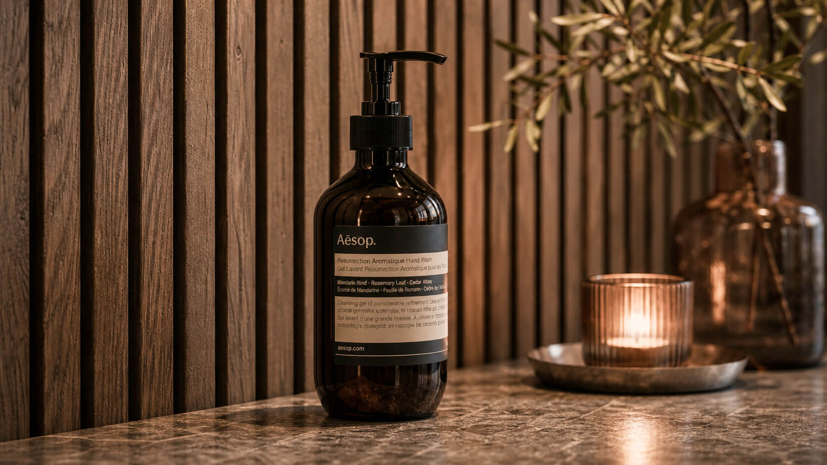 Hand soap and a lit candle beside a timber wall