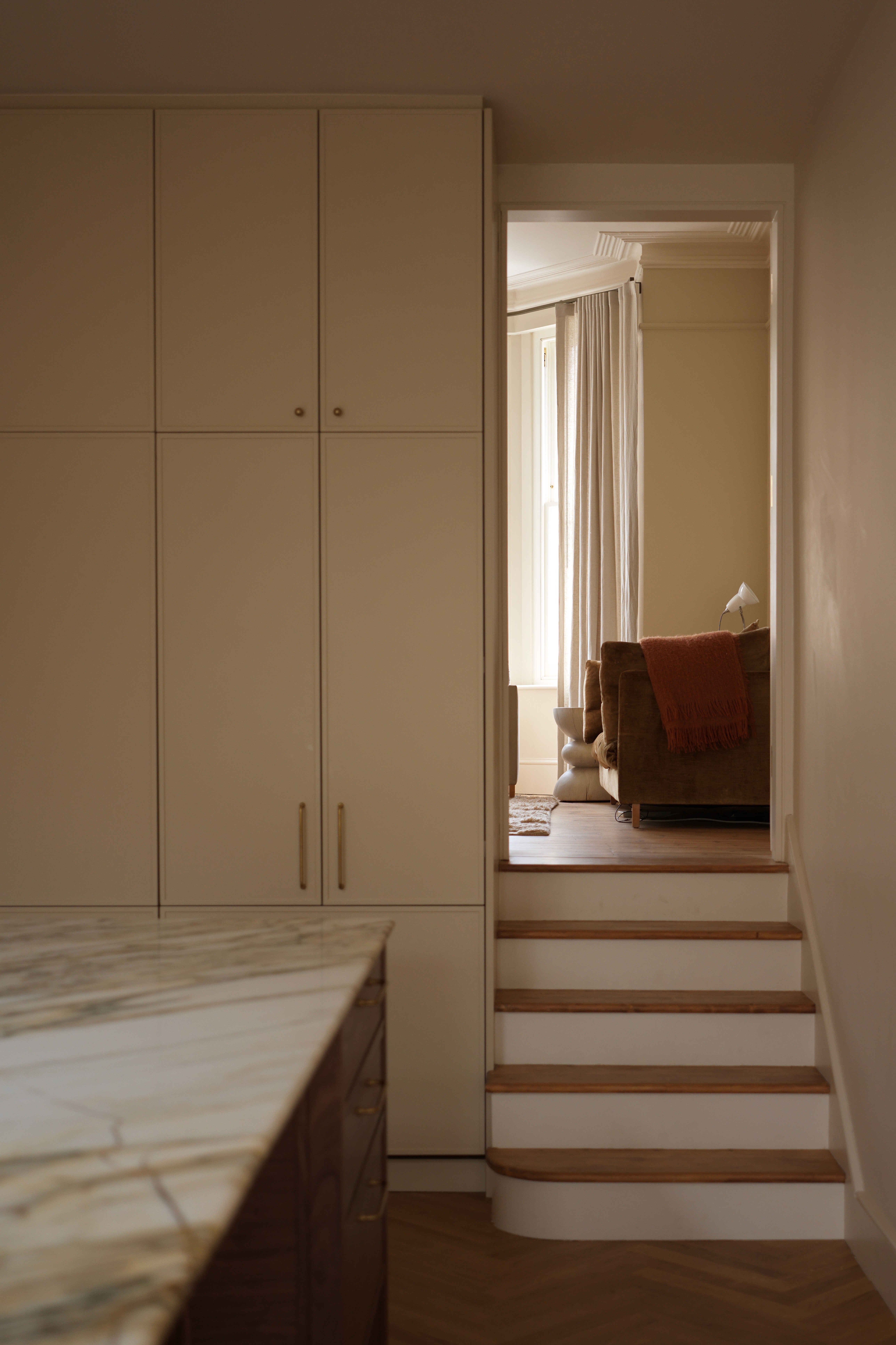 Soft neutral hallway with full-height joinery and stepped transition detail leading to the livingroom
