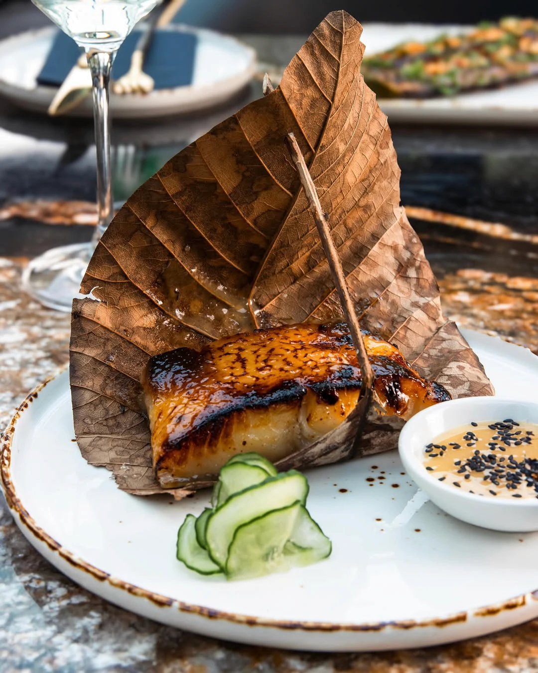 Fish dish under a large leaf with cucumber and sauce