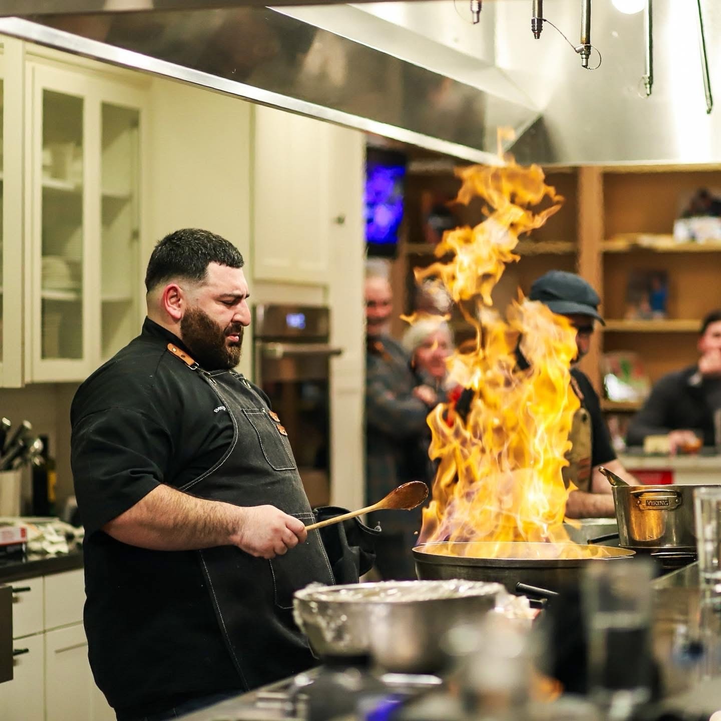Professional chef managing a large flambé flame in a kitchen