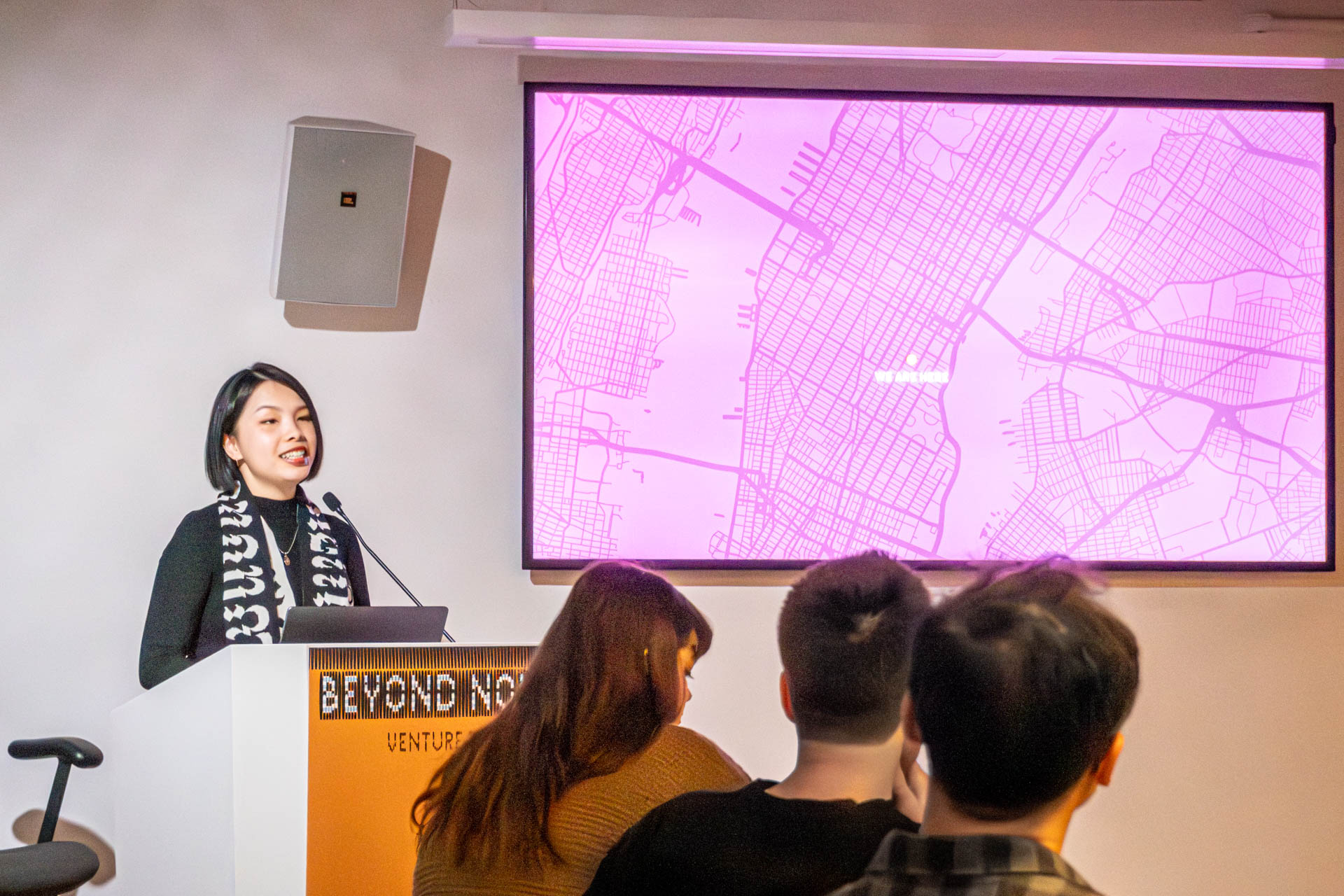 A lady at the podium giving a presentation to a class.