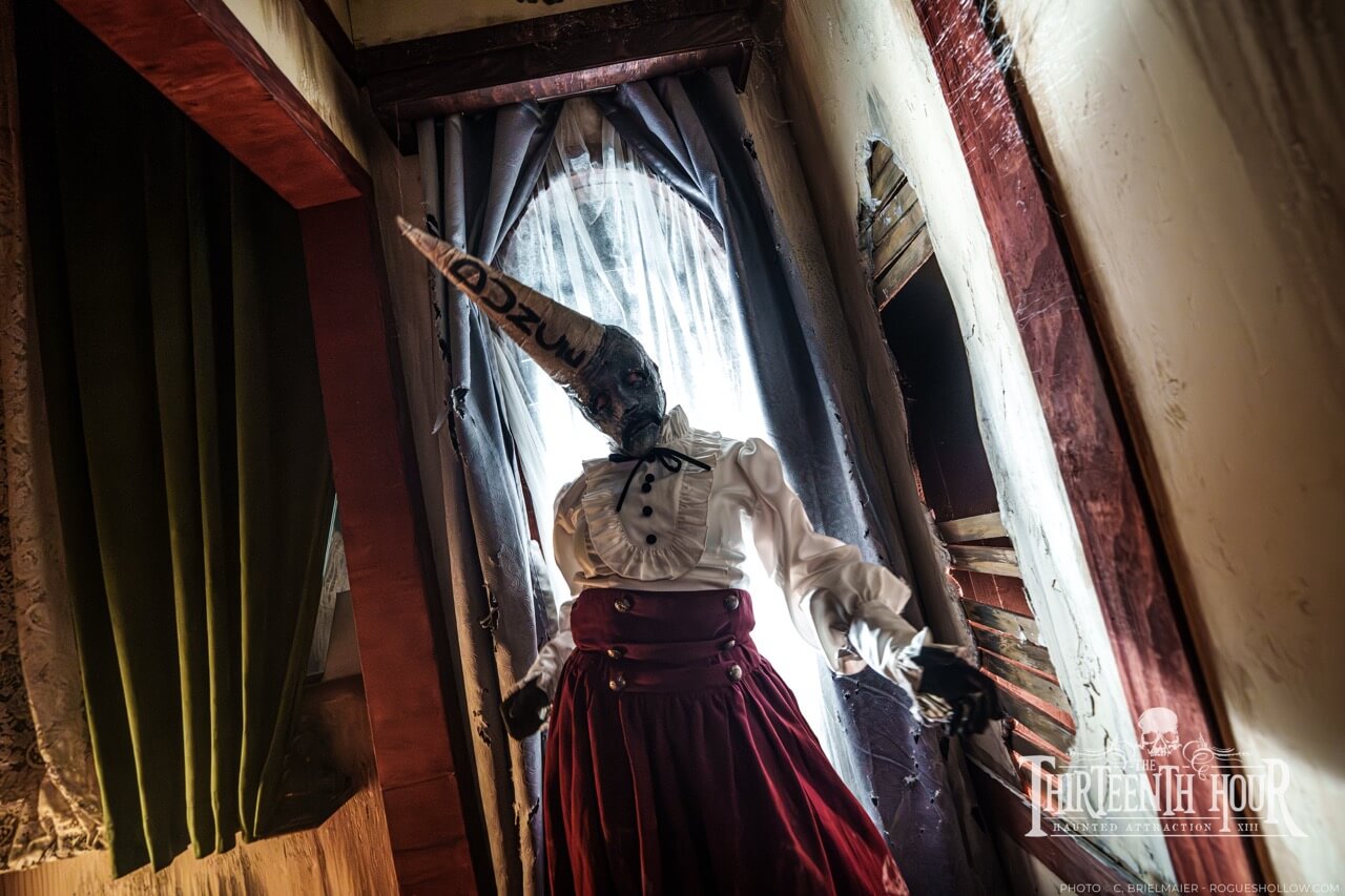 Upside-down scare actor hangs from the ceiling of a decaying bedroom set