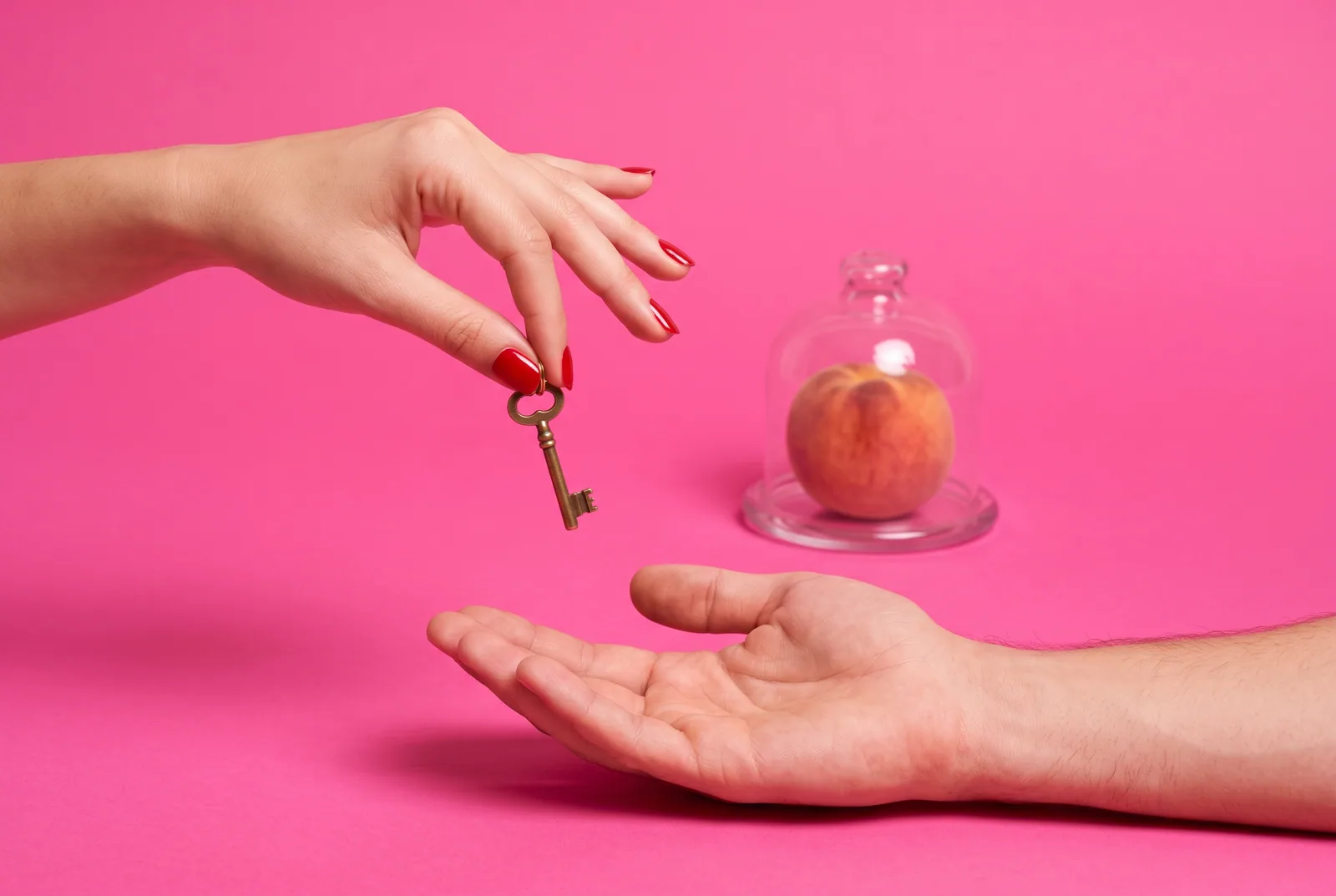 One cropped hand passing a small brass key to another hand beside a peach under a glass cloche, giving the Screen Time passcode to someone else