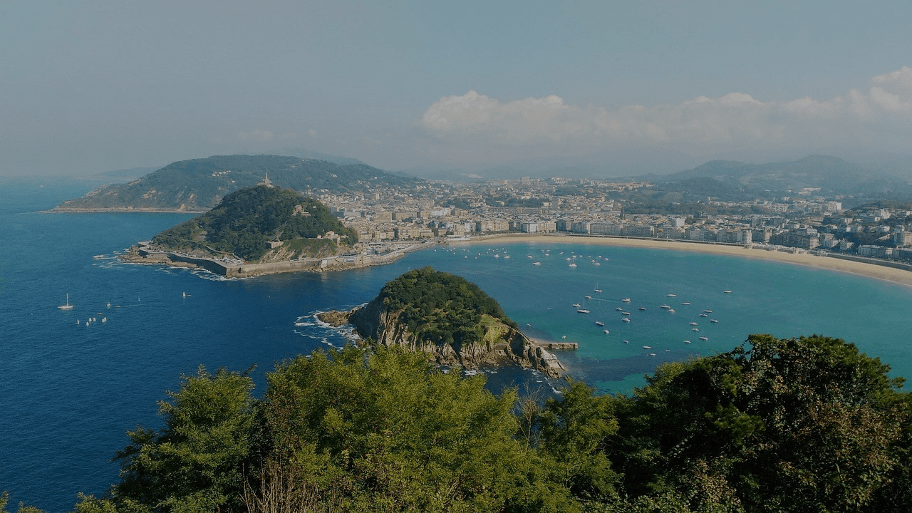 Panoramic view of San Sebastian, Spain. The city is nestled between two hills and a beautiful bay filled with boats.