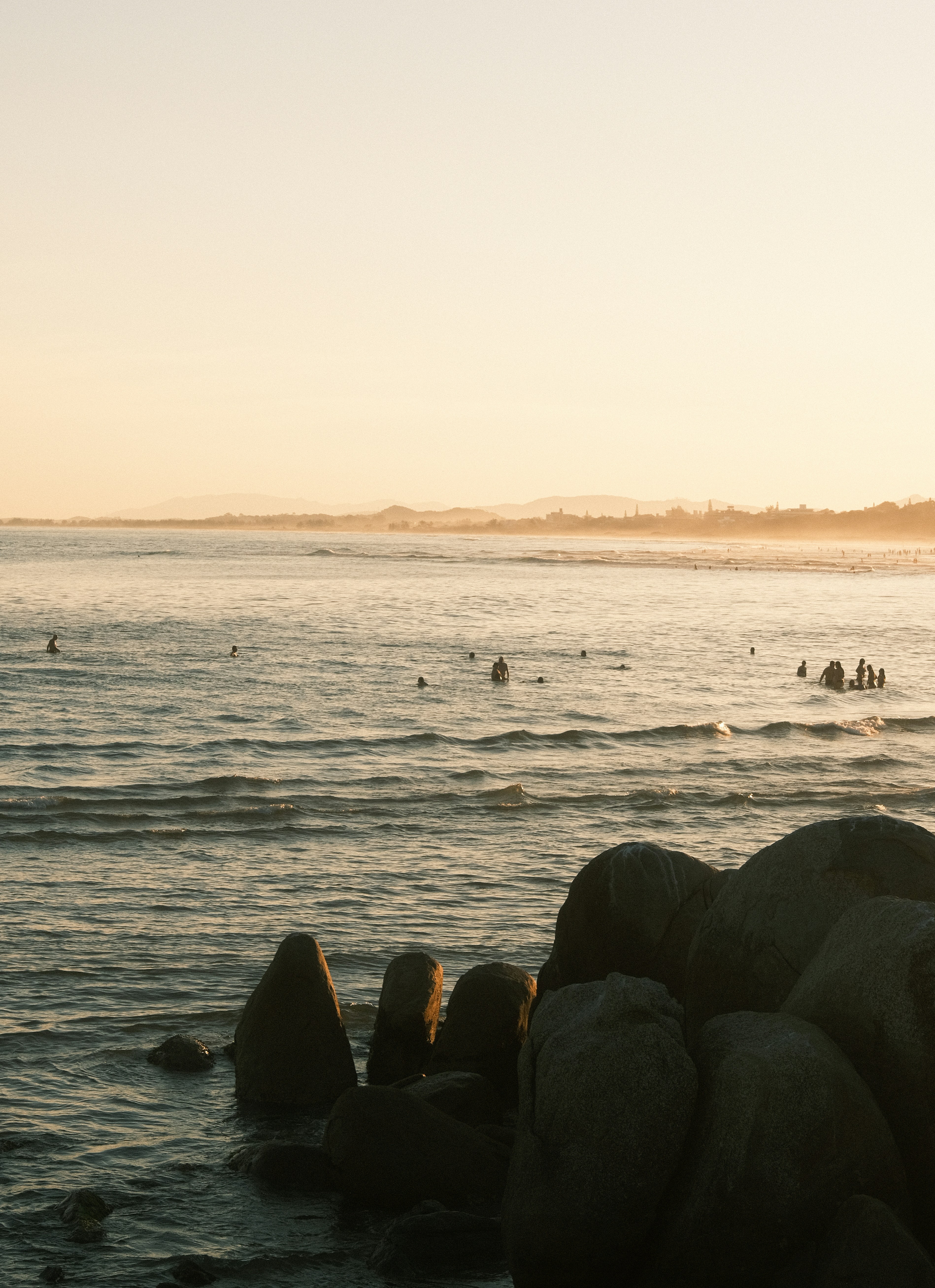 People surfing in the ocean at sunset with rocks.