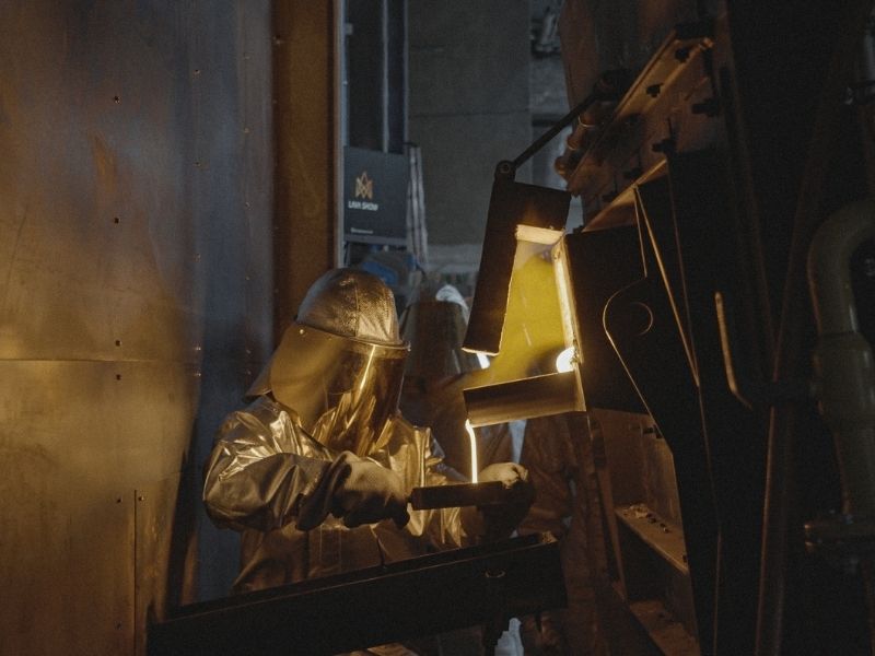 Max Greiner wears a reflective protective suit and face shield while collecting glowing molten lava from a furnace into a mould at Lava Show.