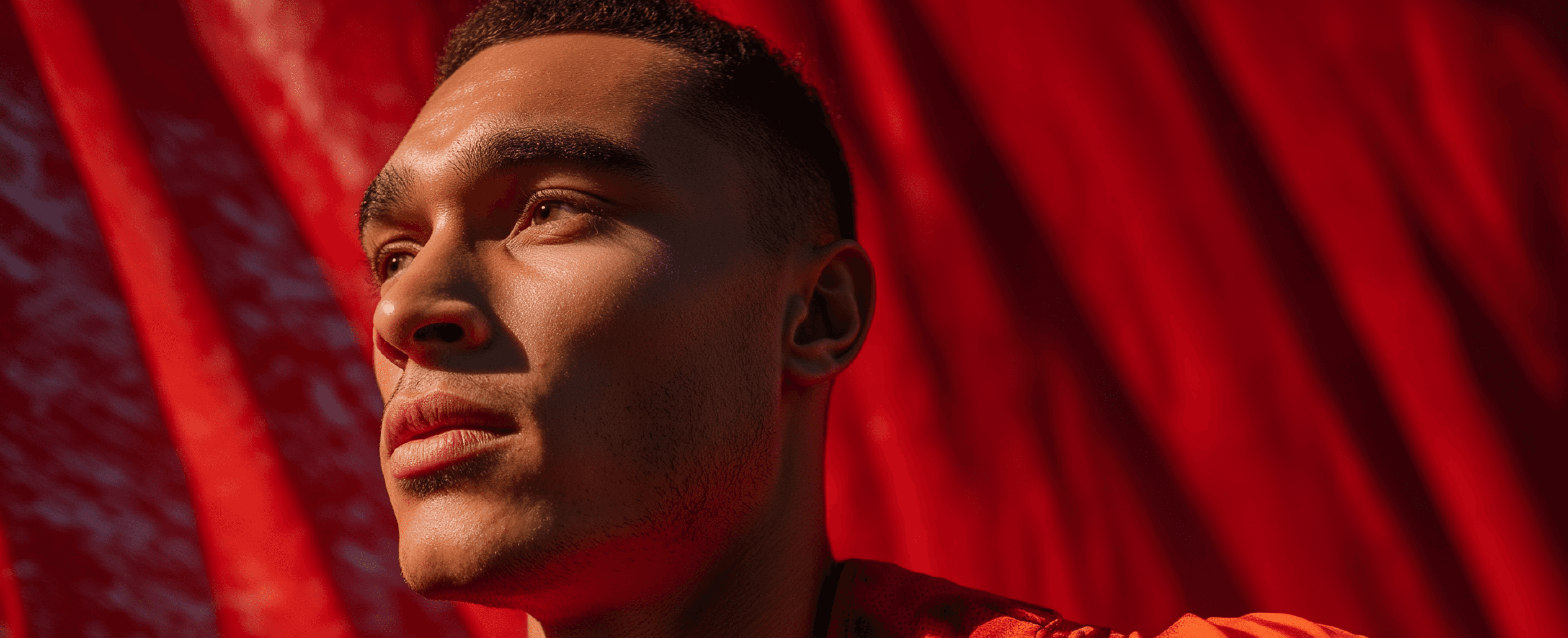 Man in profile against a red draped background with dramatic lighting.