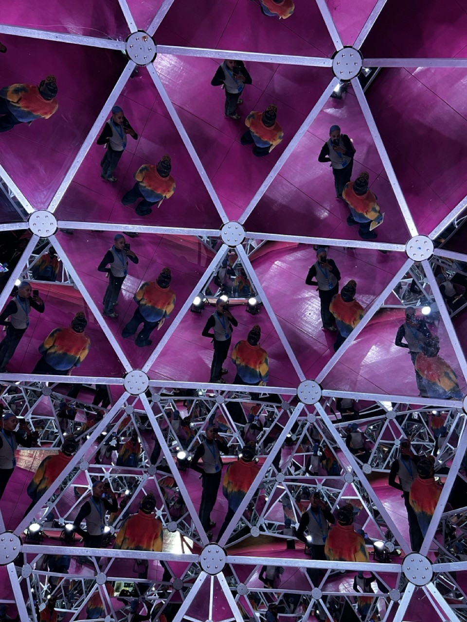 Multiple reflections of Jess captured inside a geometric mirror installation with a magenta backdrop